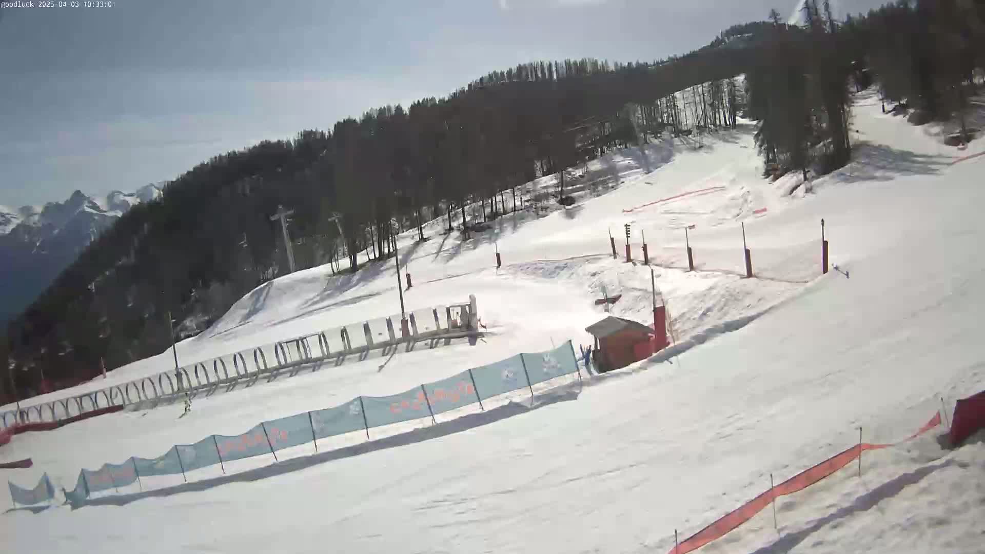 A snow-covered ski slope with a few people skiing and a sunny sky.
