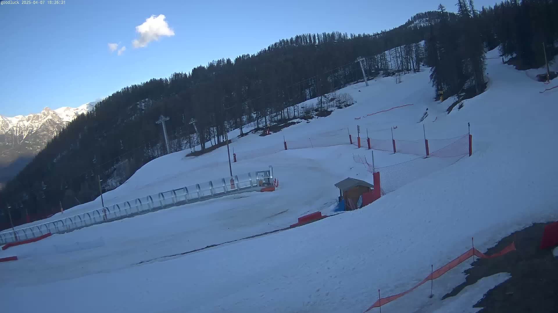 A snow-covered ski slope with ski lifts, safety nets, and a small building is visible under a clear, bright sky.