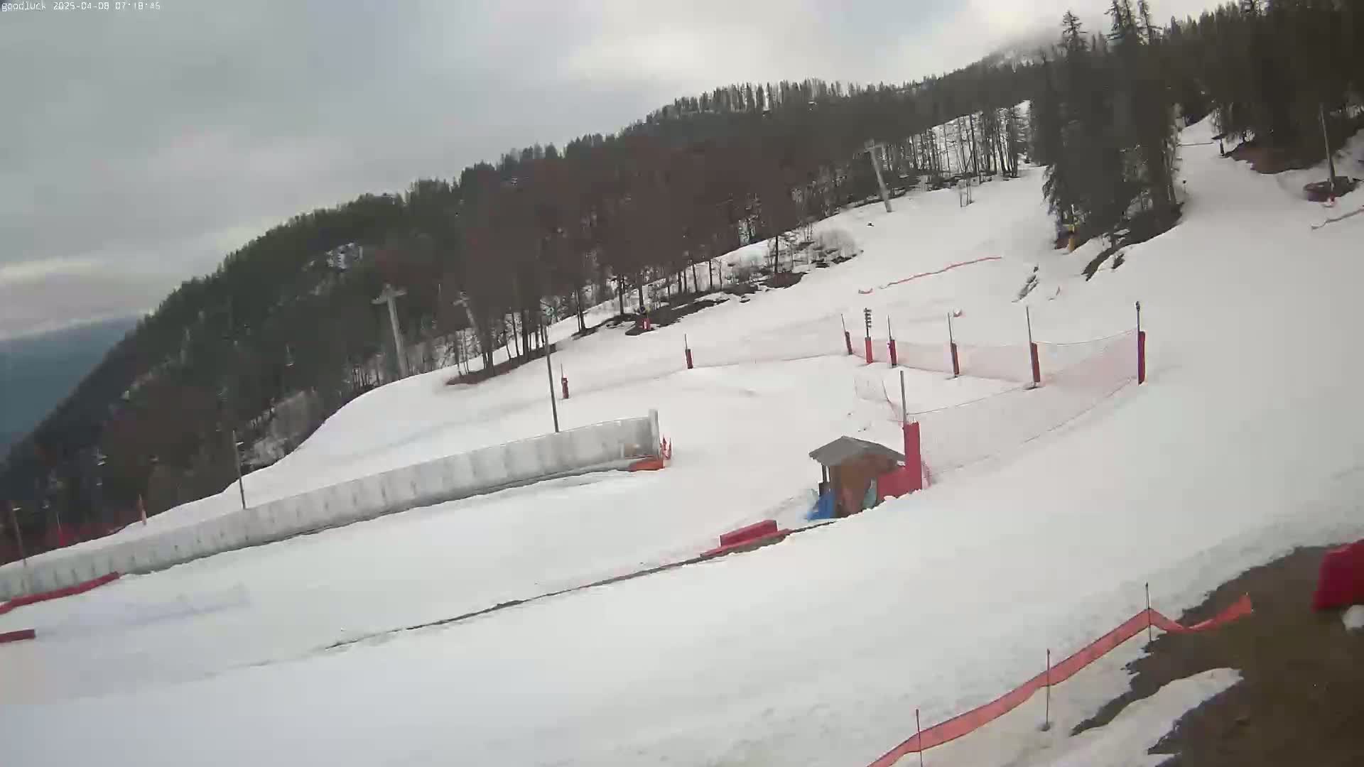 A snow-covered ski slope with safety nets and a small building is visible under an overcast sky.