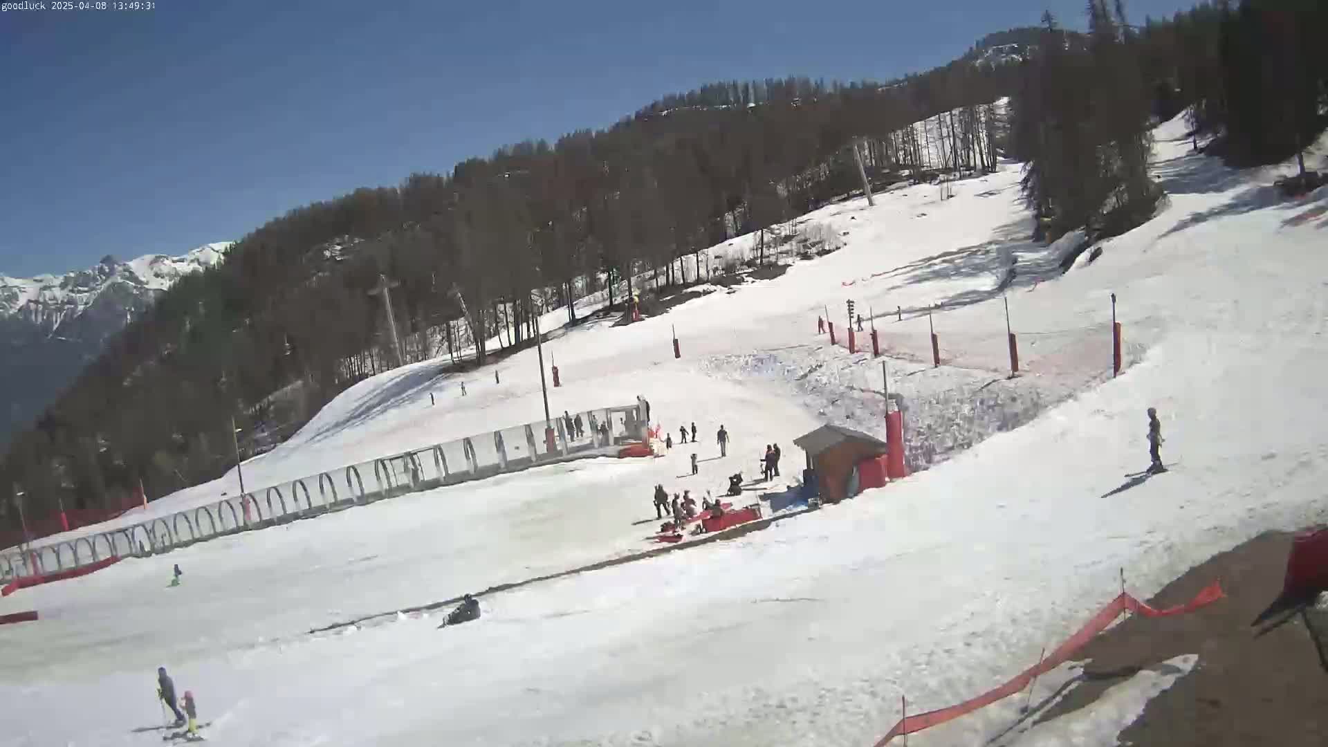A snowy ski slope with several skiers and onlookers under a clear blue sky.
