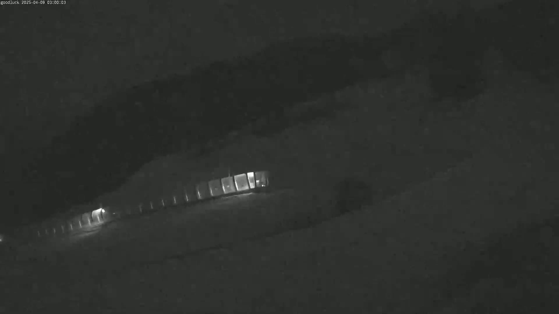 A long, low building with illuminated windows is visible at night in snowy conditions.