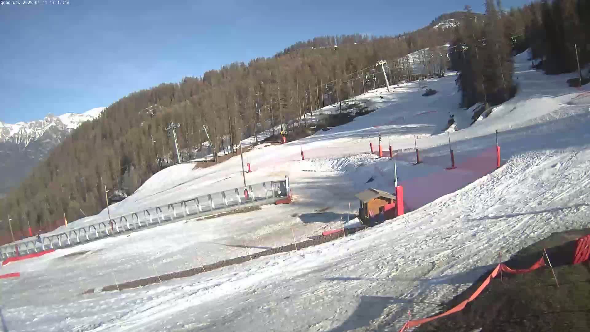 A snow-covered ski slope with a ski lift and surrounding trees under a clear, sunny sky.