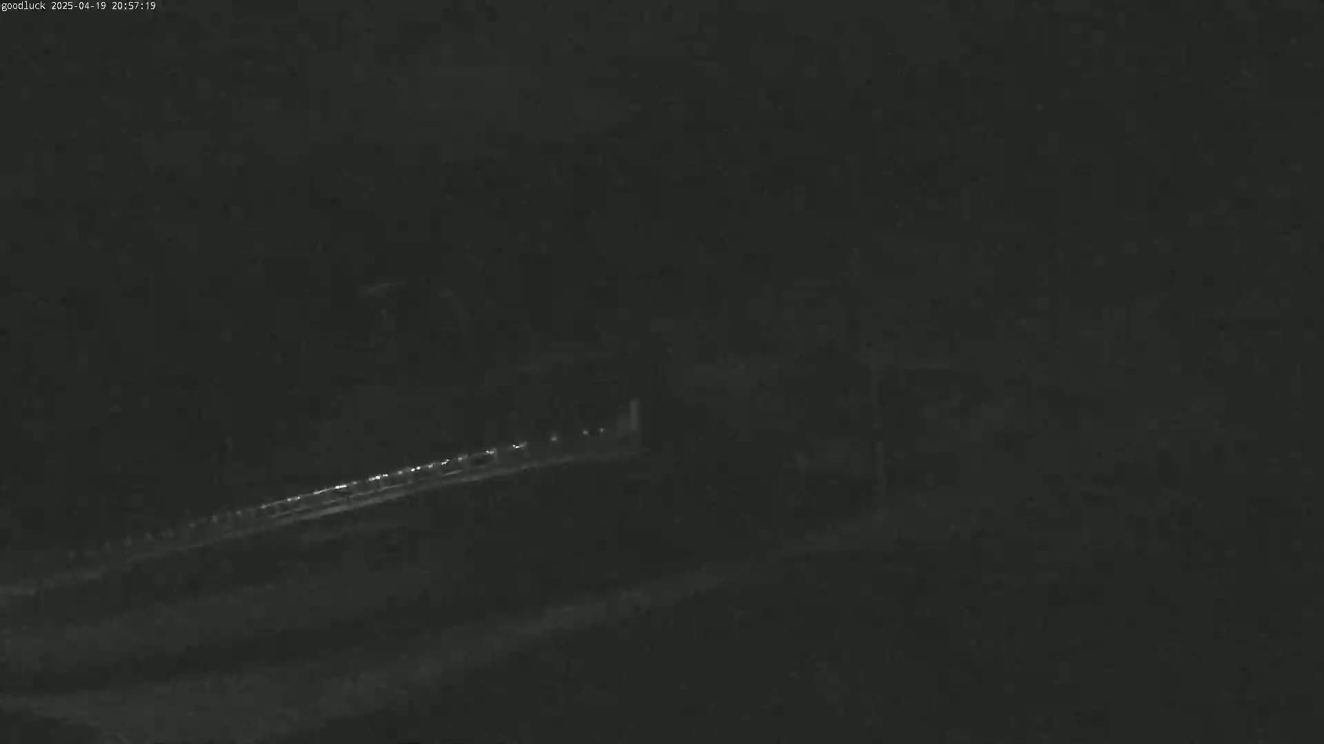 A blurry, low-light image shows a dark roadway with faint lights in the distance at night.