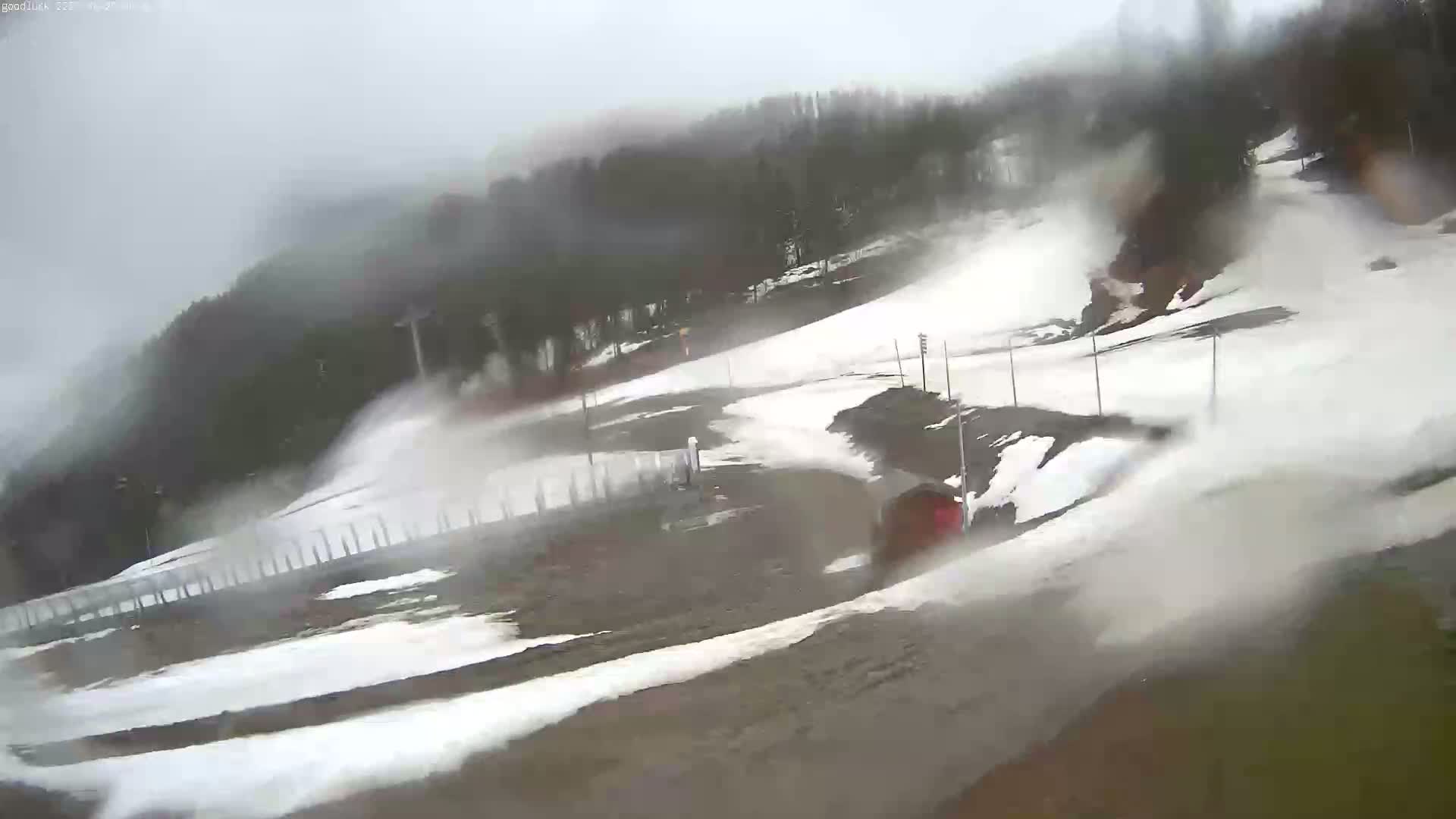 A snow-covered ski slope is visible through heavy rain, with a vehicle partially obscured by the downpour near the bottom.