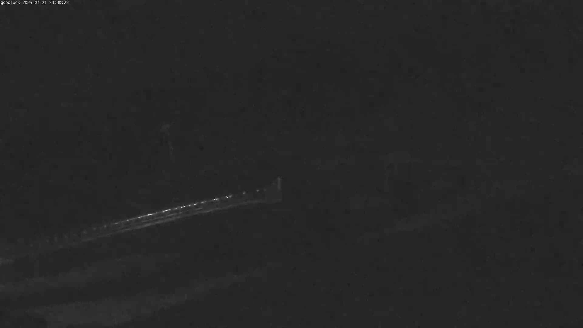 A dimly lit, nighttime scene shows a long, thin line of lights in the distance, possibly a road or bridge.