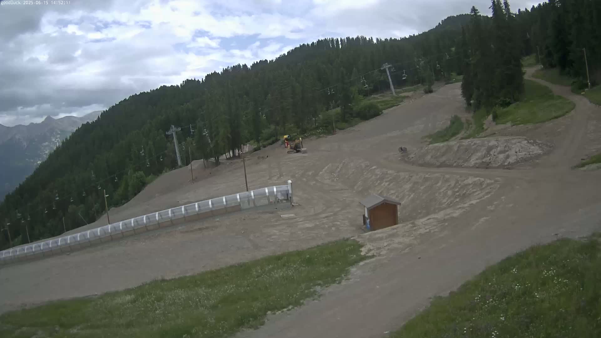 A mostly cloudy day overlooks a mountainside ski slope with several chairlifts, some construction equipment, and a small building.