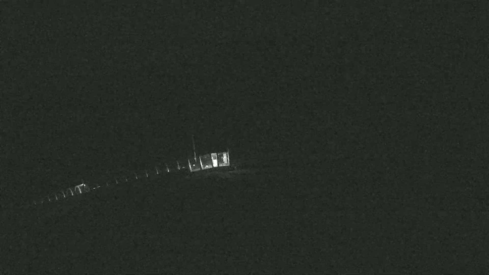 A long, low-lying structure with illuminated windows is visible at night.