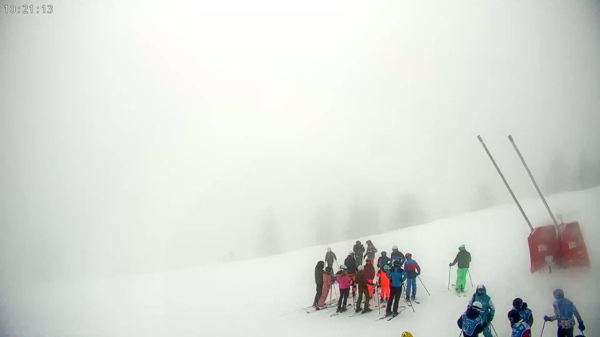 A group of skiers and snowboarders stands on a snowy slope in heavy fog.