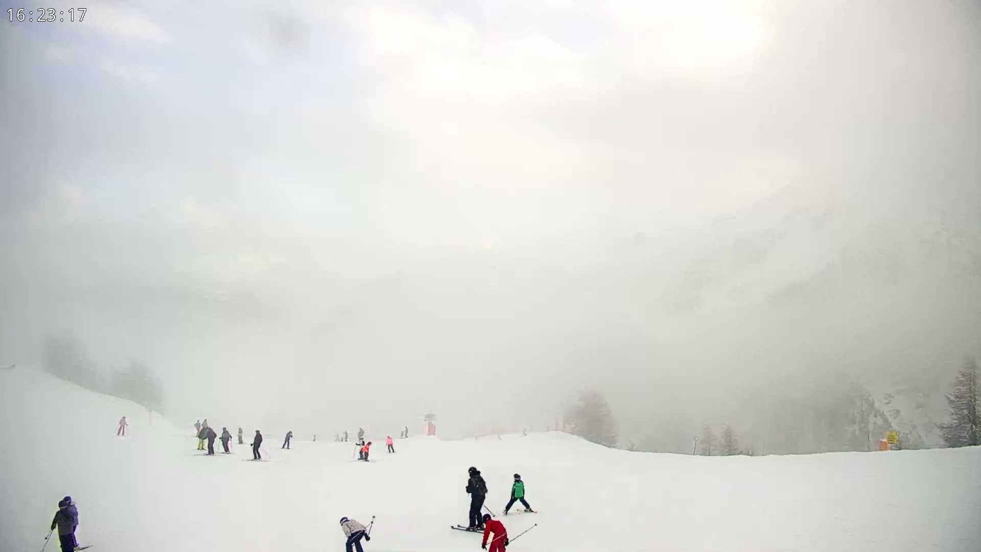 A snowy ski slope is visible through a thick fog, with several skiers scattered across the expanse.