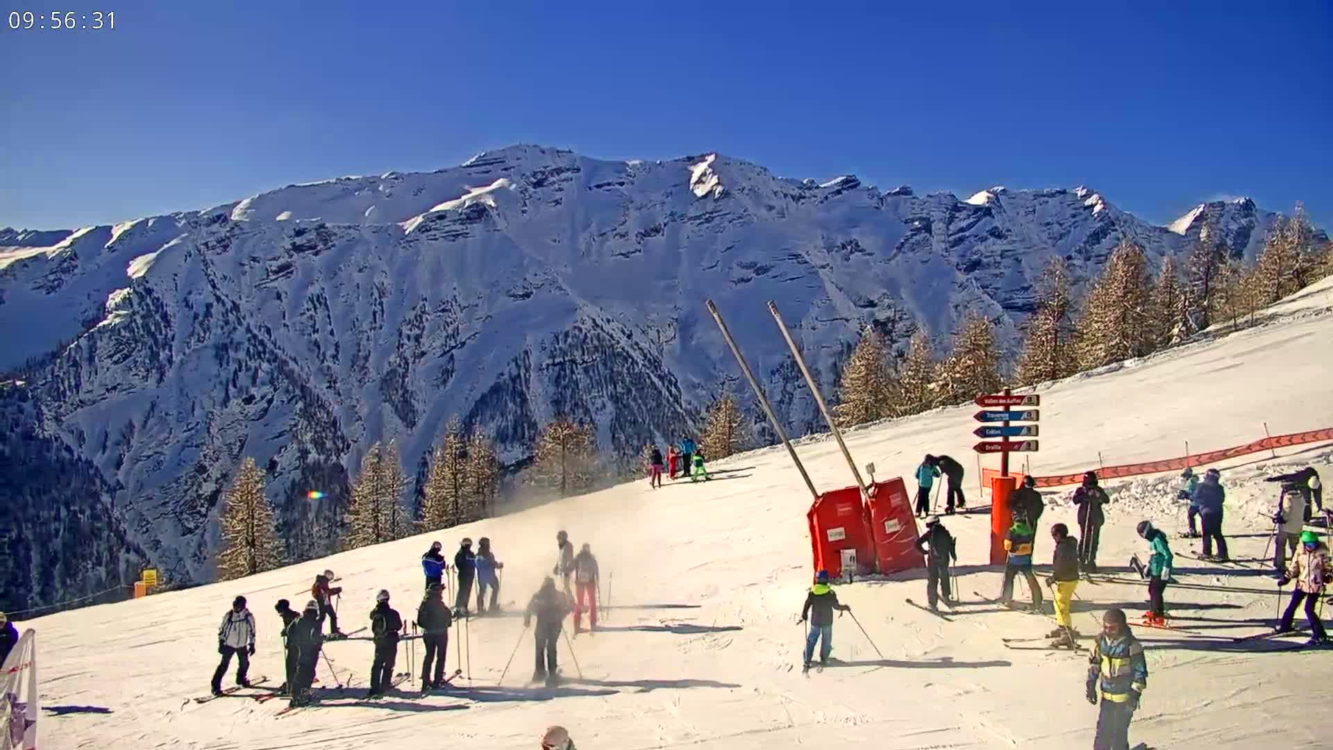 A sunny day on a snow-covered ski slope with skiers and snowboarders,  set against a backdrop of snow-capped mountains.