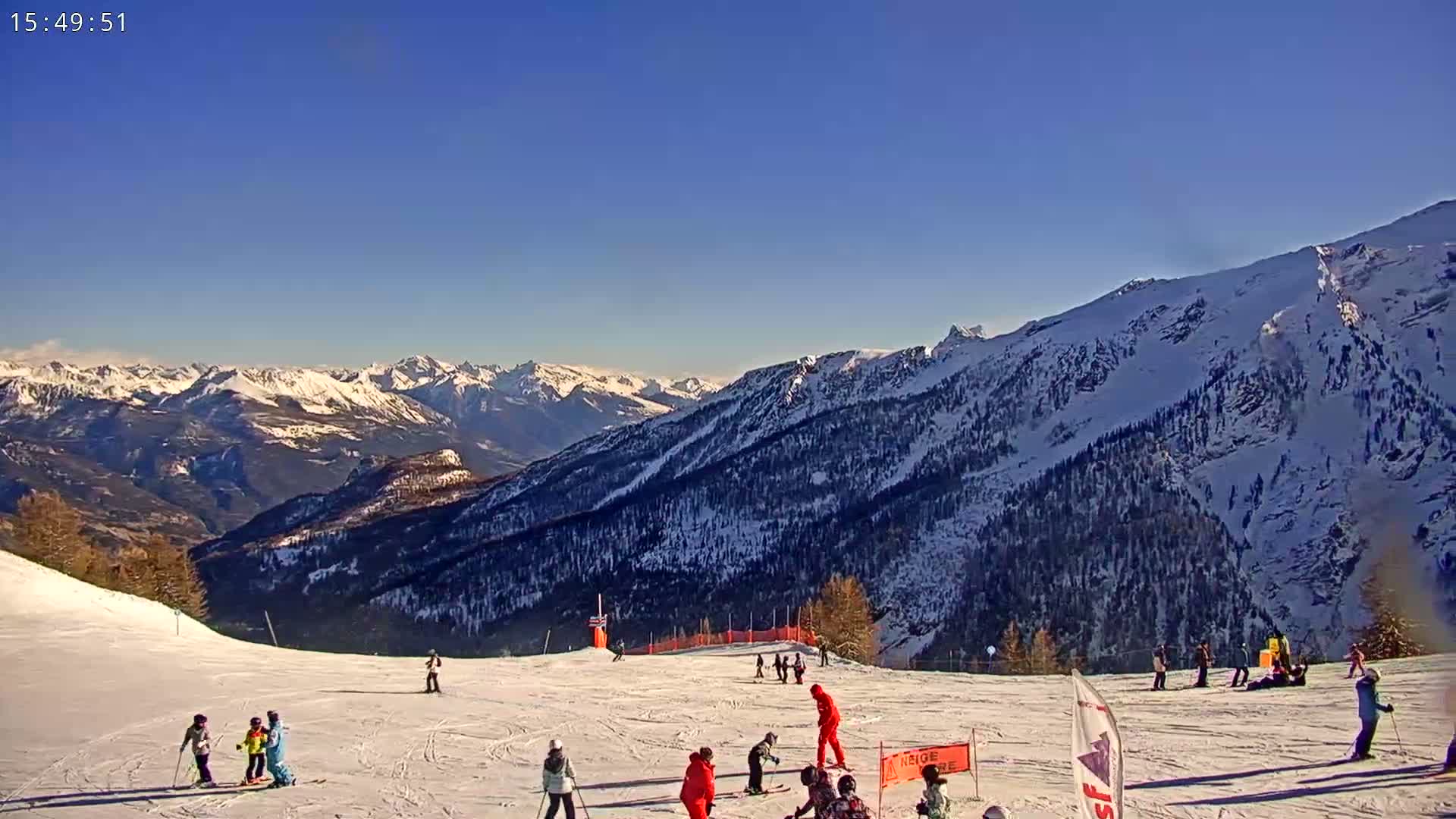A sunny day on a snow-covered ski slope with skiers and snowboarders enjoying the mountain view.