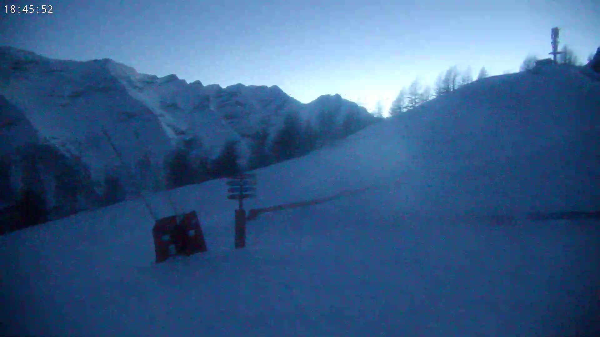 A snow-covered ski slope at dusk, with mountains in the background under a twilight sky.