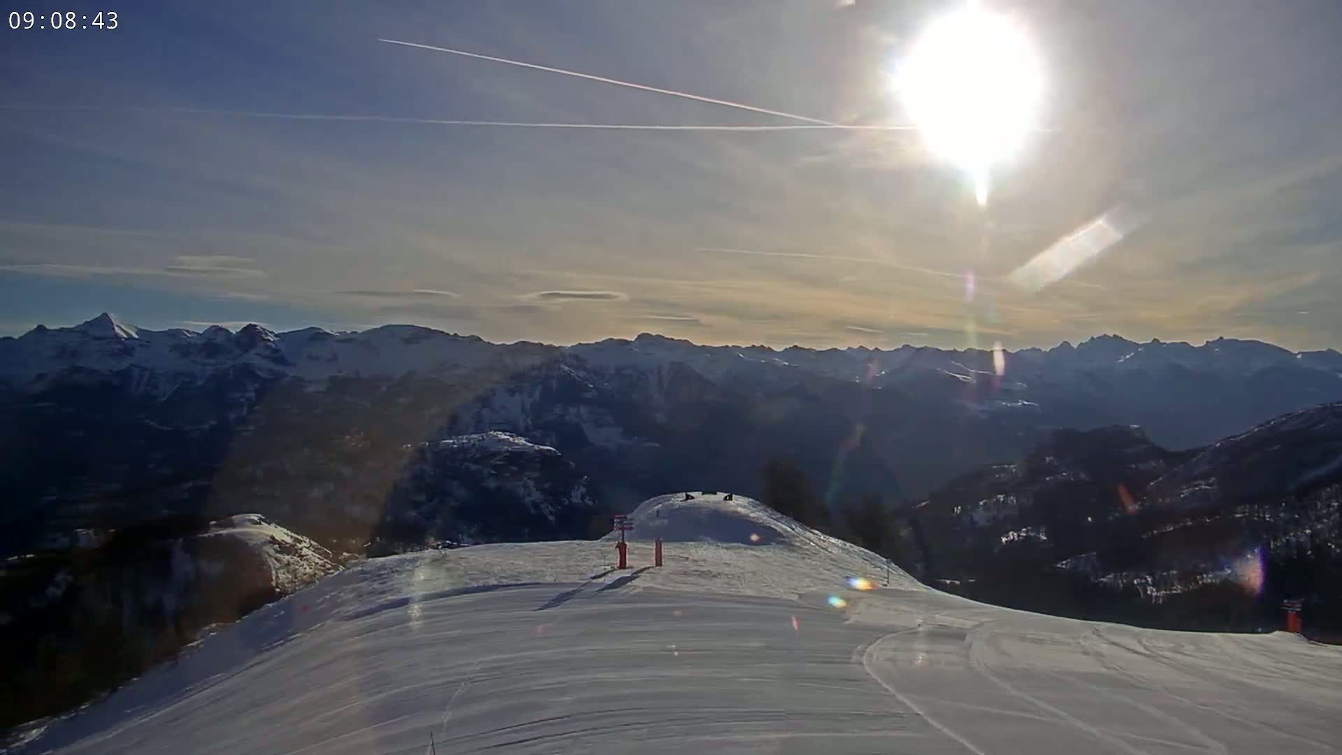 A sunny day reveals a snow-covered mountain slope overlooking a vast range of snow-capped mountains.
