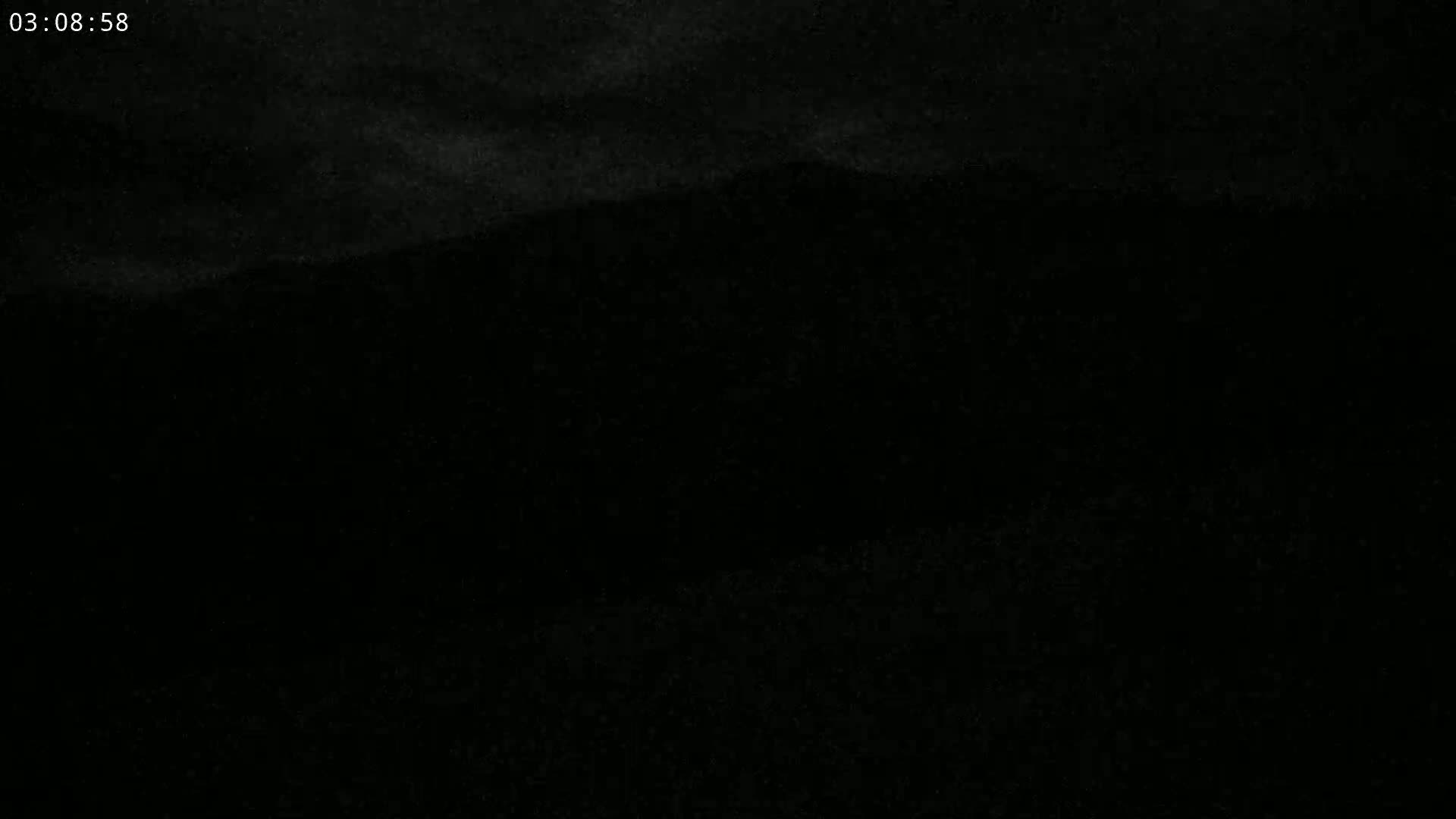 A dark, nighttime scene shows a dimly lit landscape under a cloudy sky.