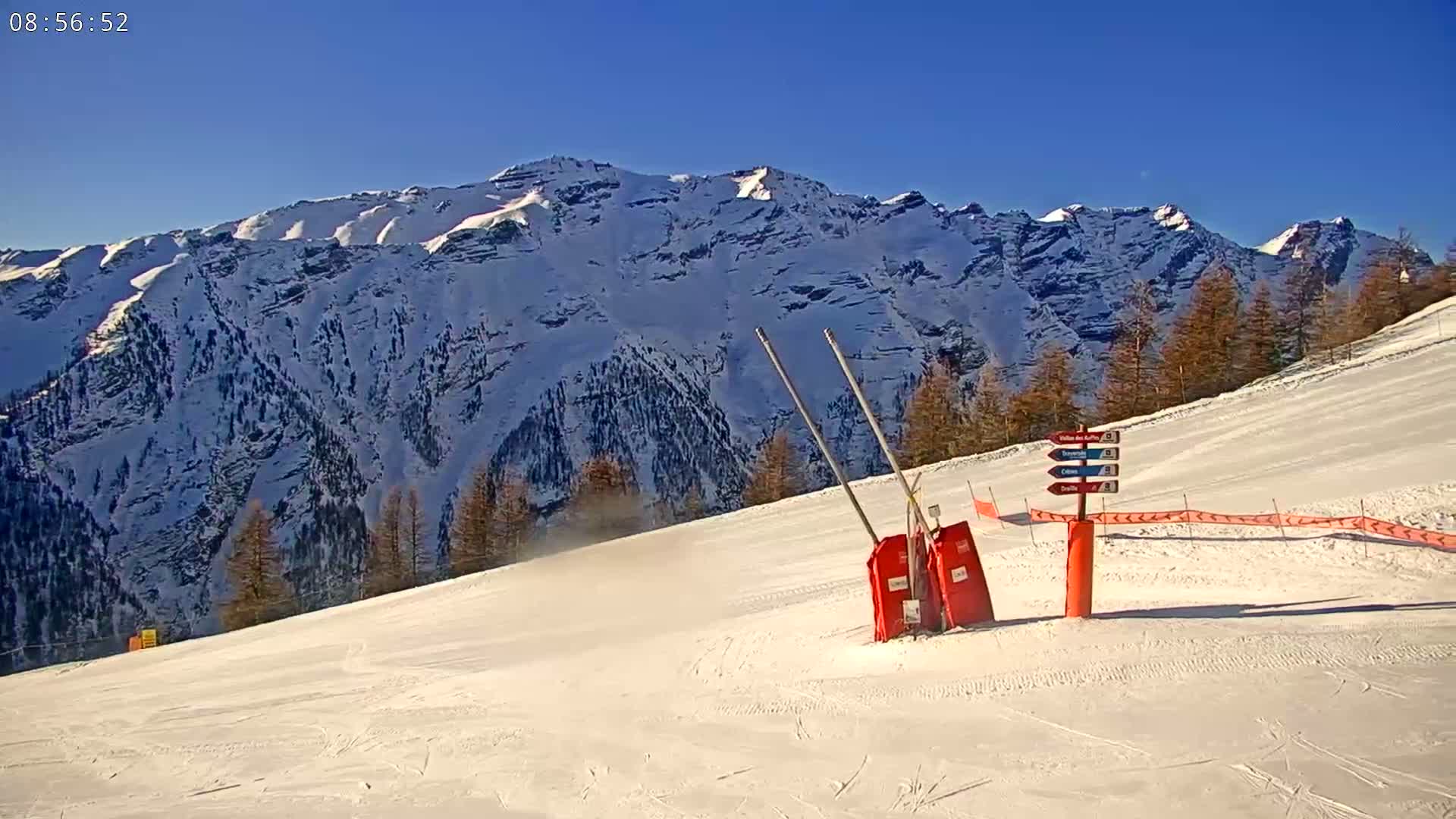 A snow-covered ski slope with a mountain range in the background under a clear blue sky.