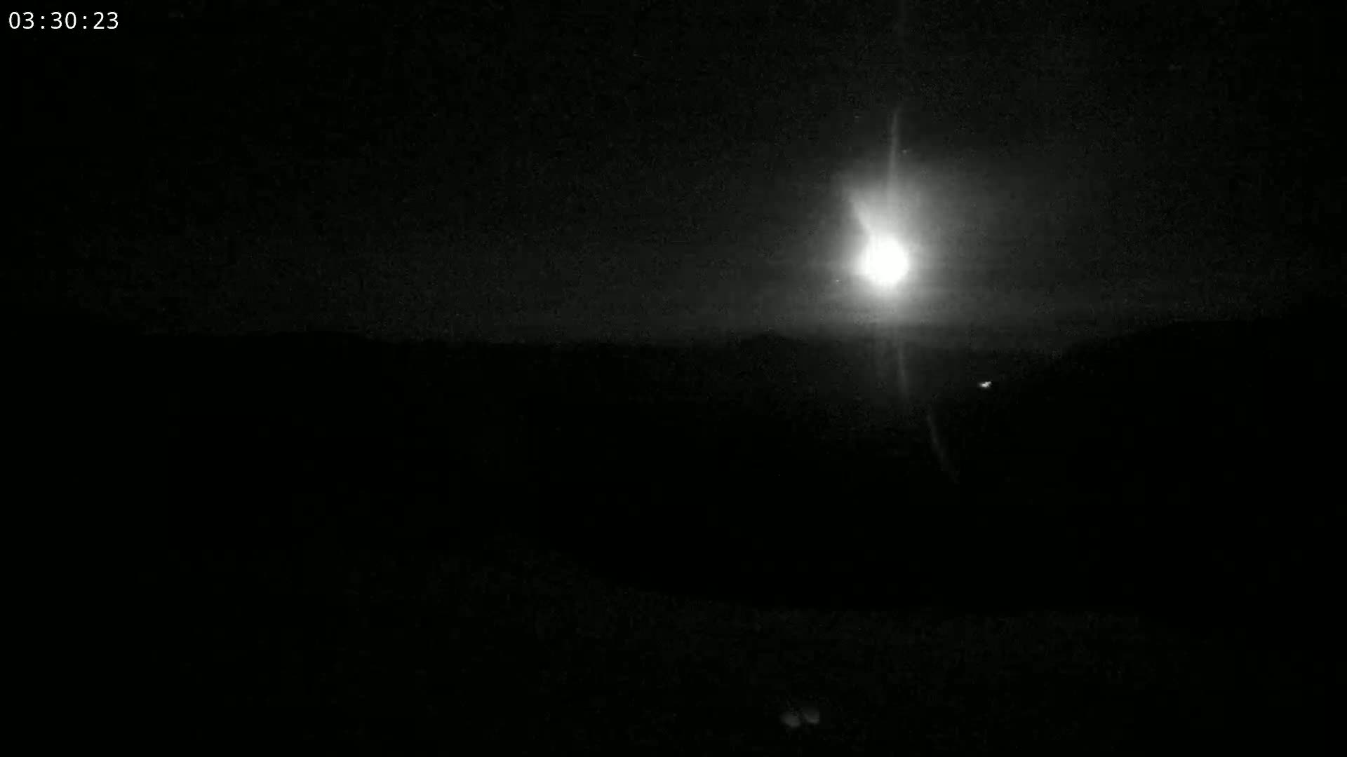 A bright moon shines over a dark, flat landscape at night.