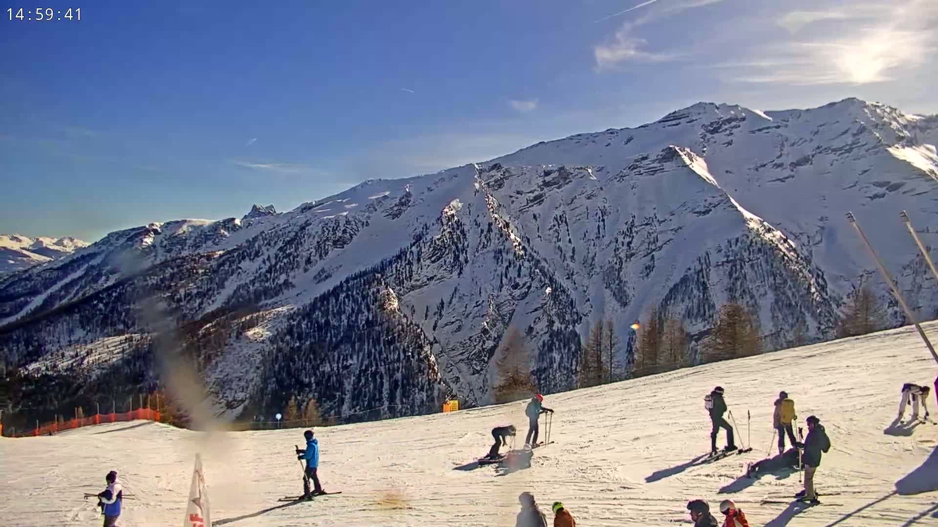 A sunny day on a snow-covered ski slope with skiers and snowboarders enjoying the mountain view.