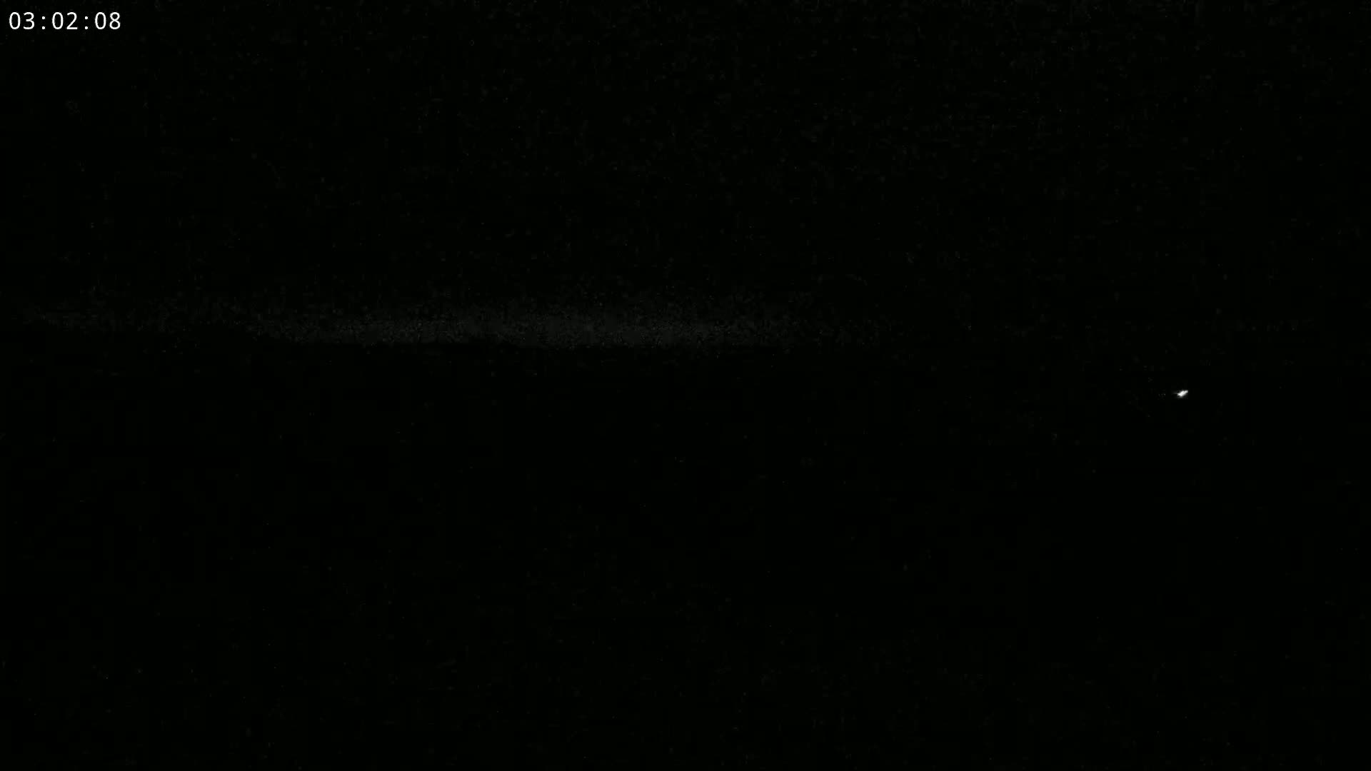 A nighttime, dark image shows a faint, horizontal line of light near the bottom, with a single, brighter light near the right side.
