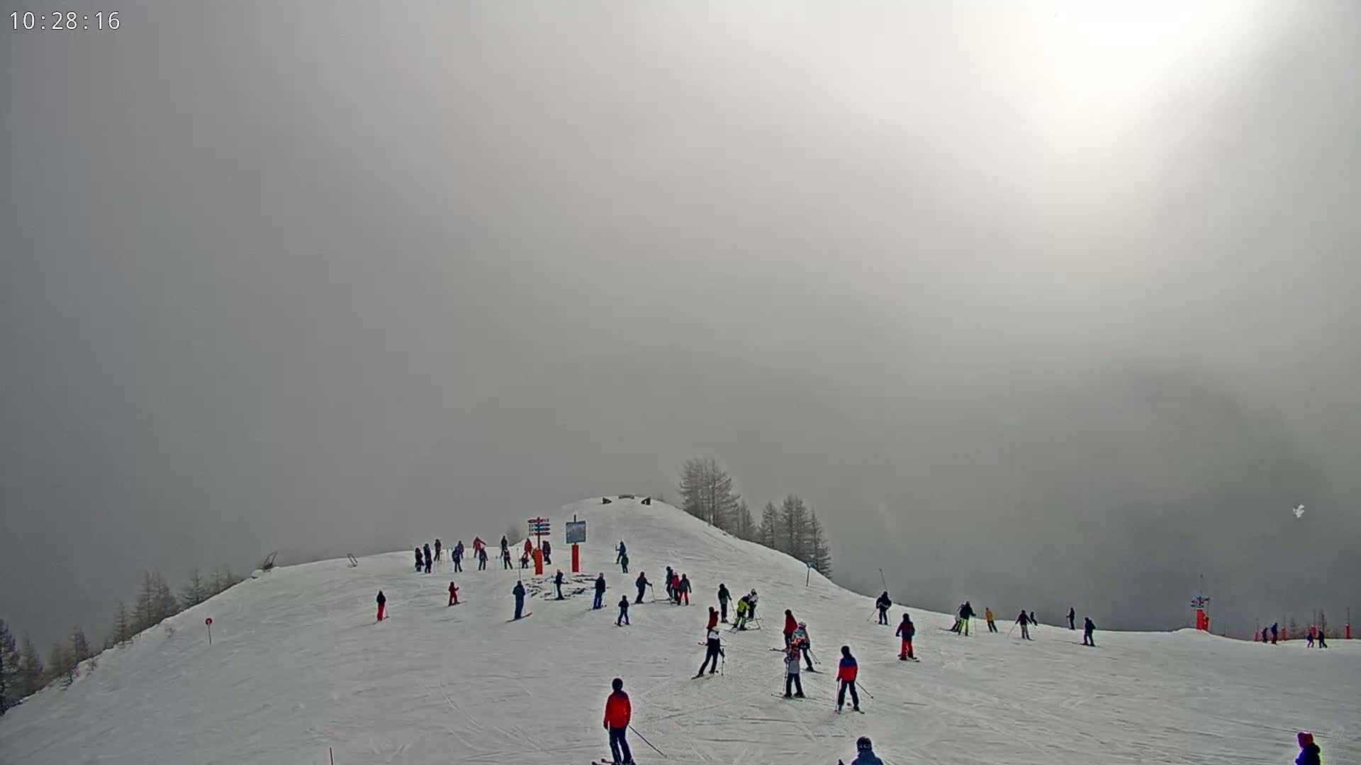 A snowy ski slope on a foggy day, with several skiers scattered across the incline.