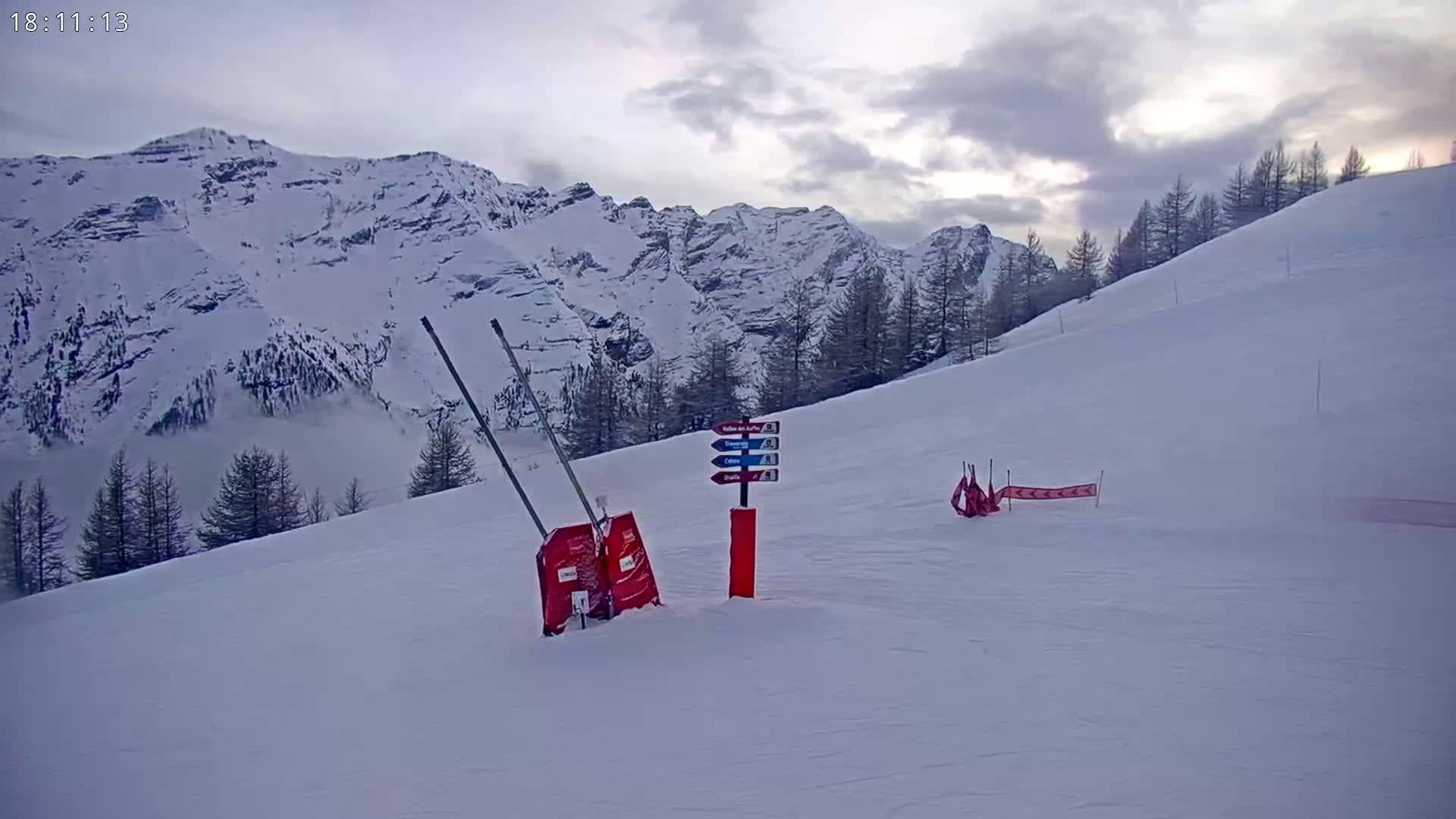 A snowy mountain slope with a trail marker and ski lift gates, under an overcast sky.