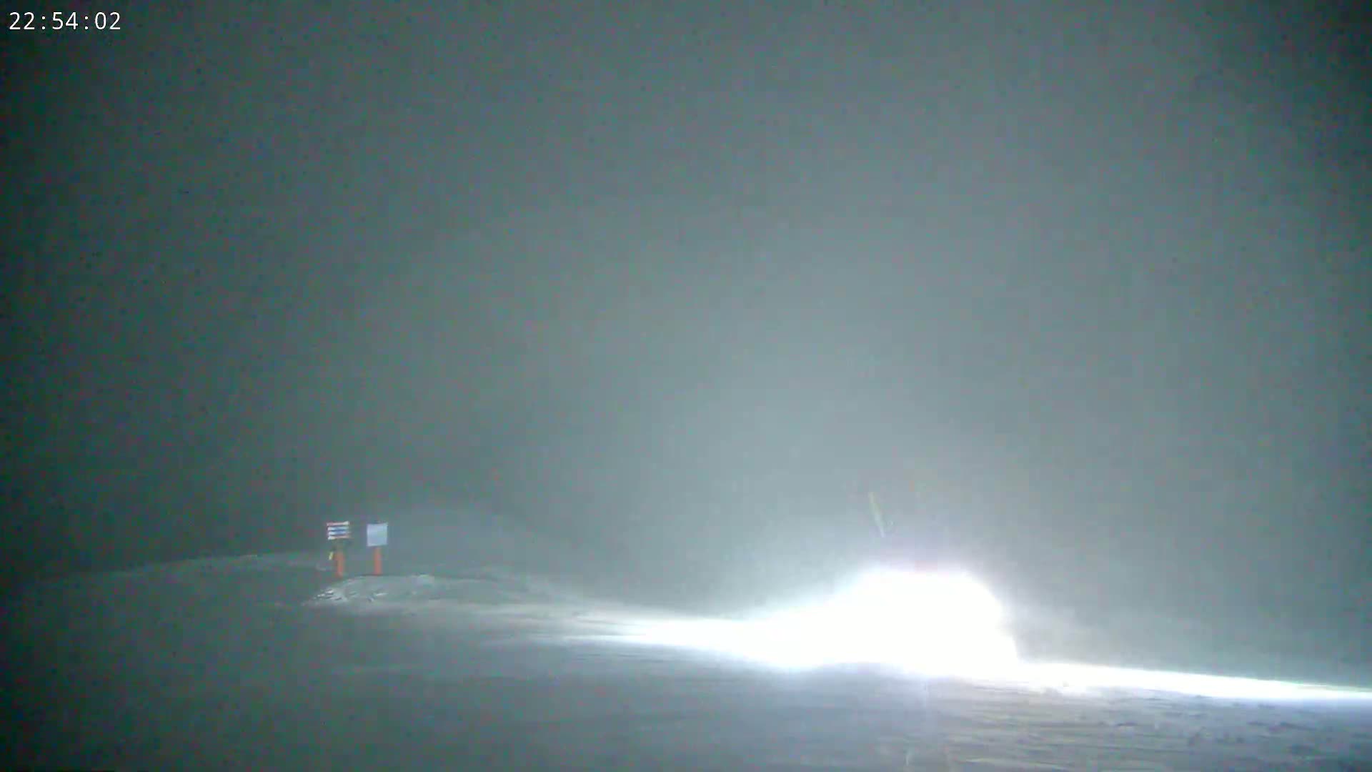 A vehicle's headlights illuminate a snowy, foggy landscape at night.