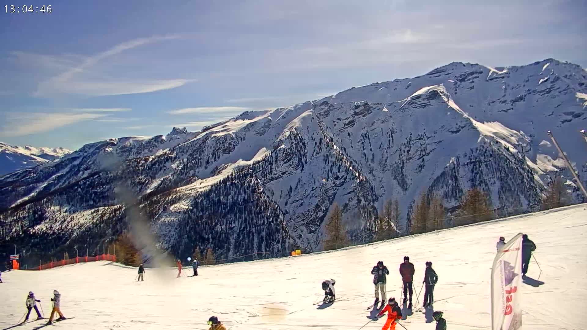A sunny day on a snow-covered ski slope with skiers and snowboarders enjoying the mountain views.