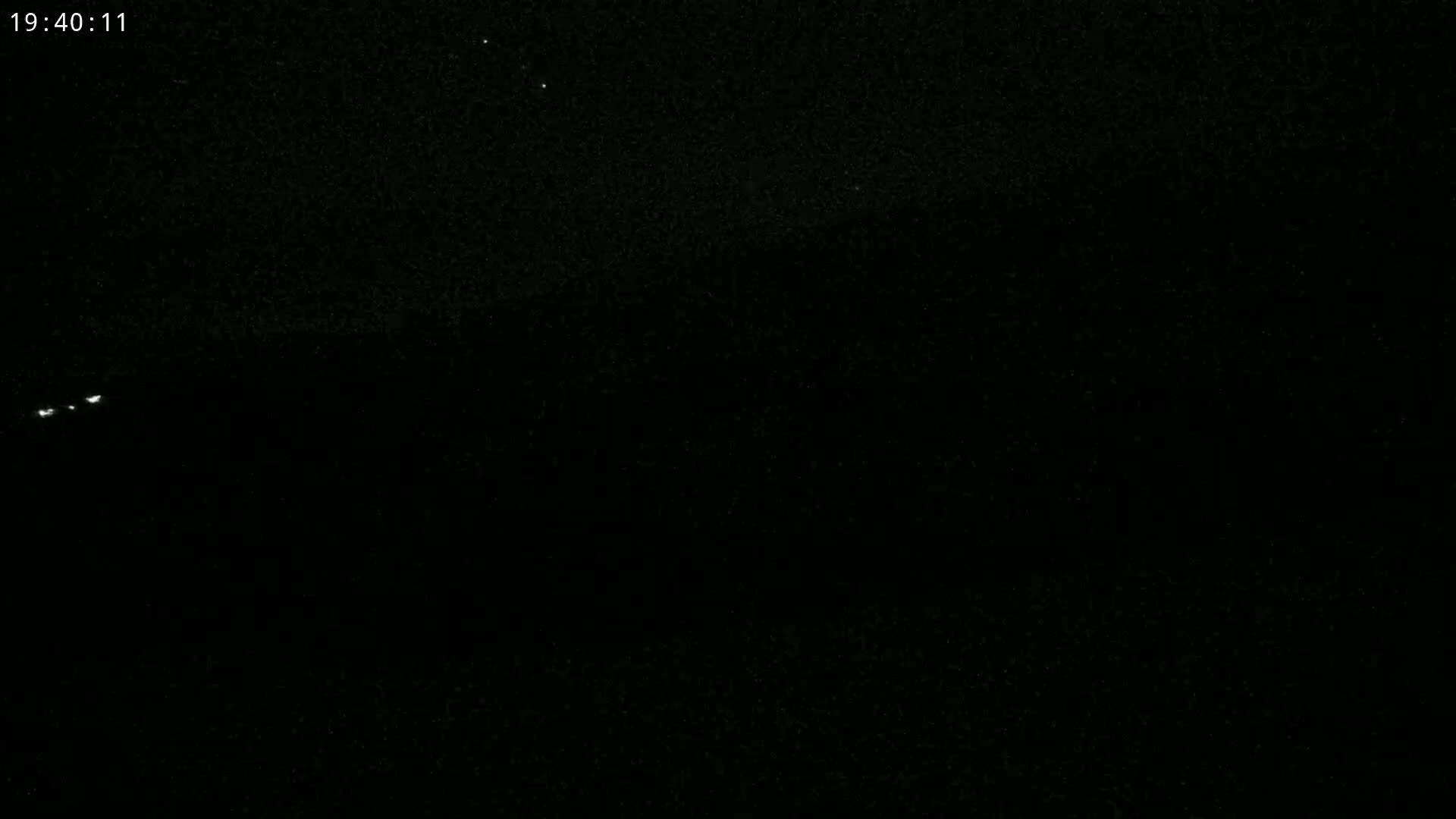 A nighttime, dark image shows a few faint lights in the distance under a clear, star-studded sky.