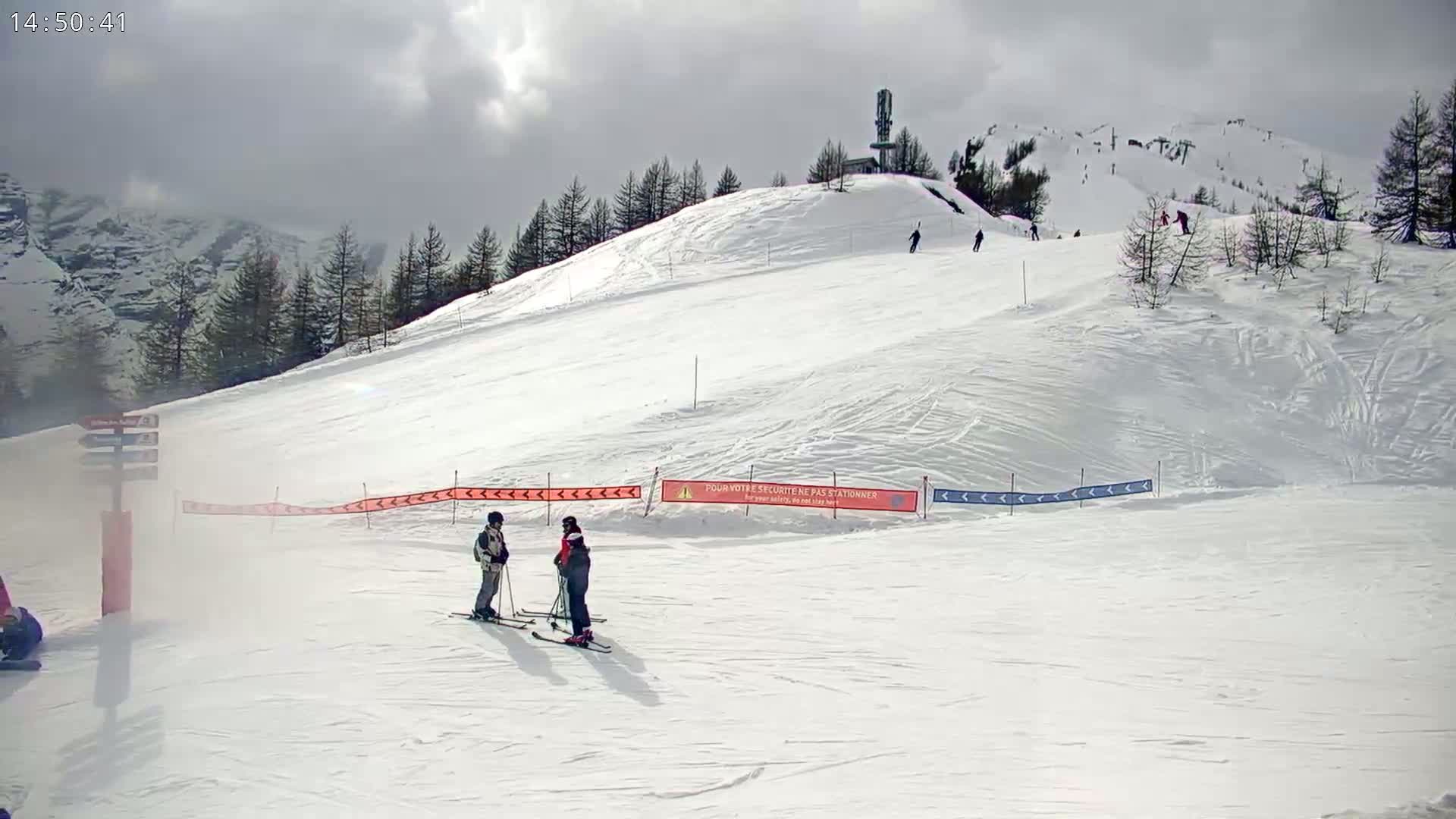A snowy ski slope with a few skiers, under a cloudy sky.