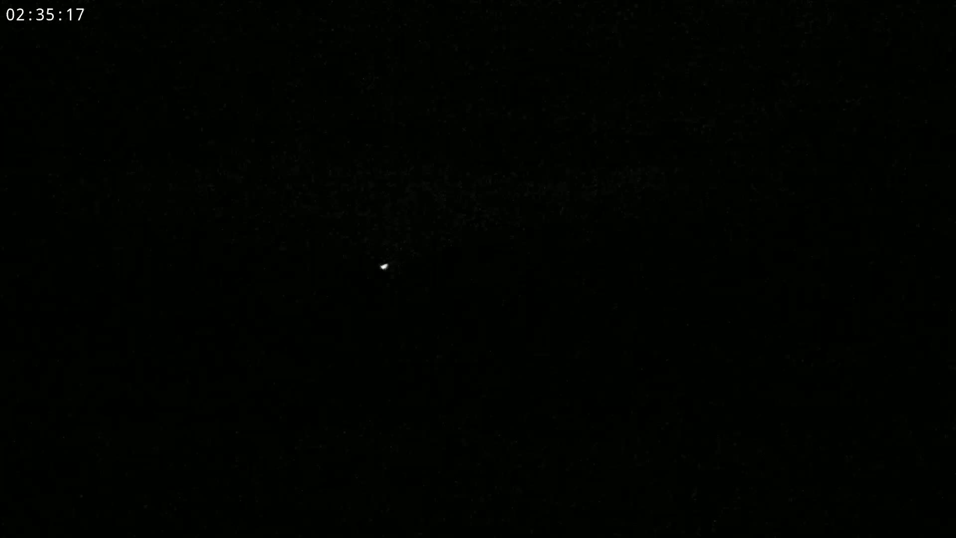 A tiny, bright light is visible in the center of a completely dark, nighttime sky.