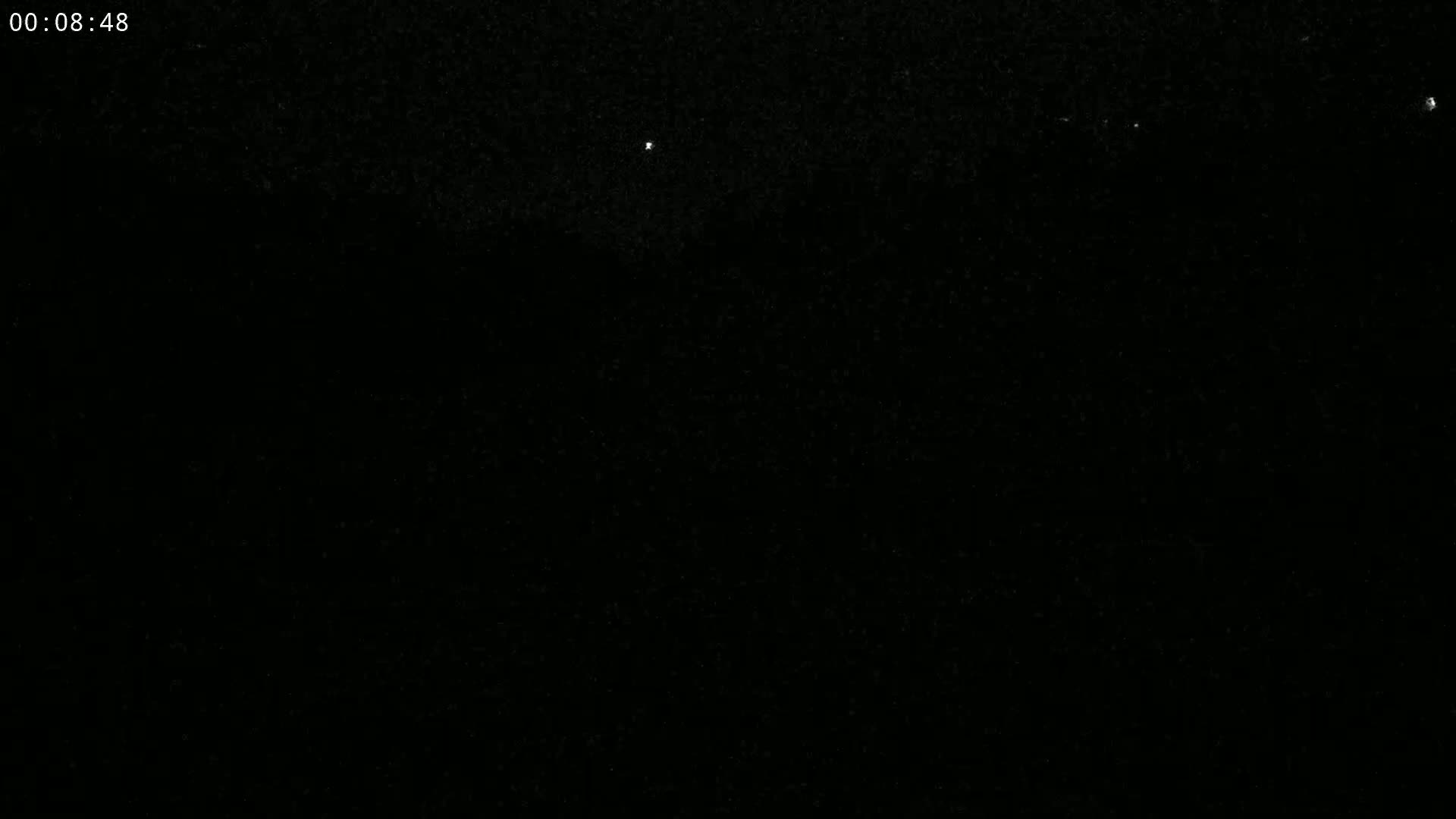 A dark, nighttime scene shows a few faint lights in the distance against a mostly black sky.