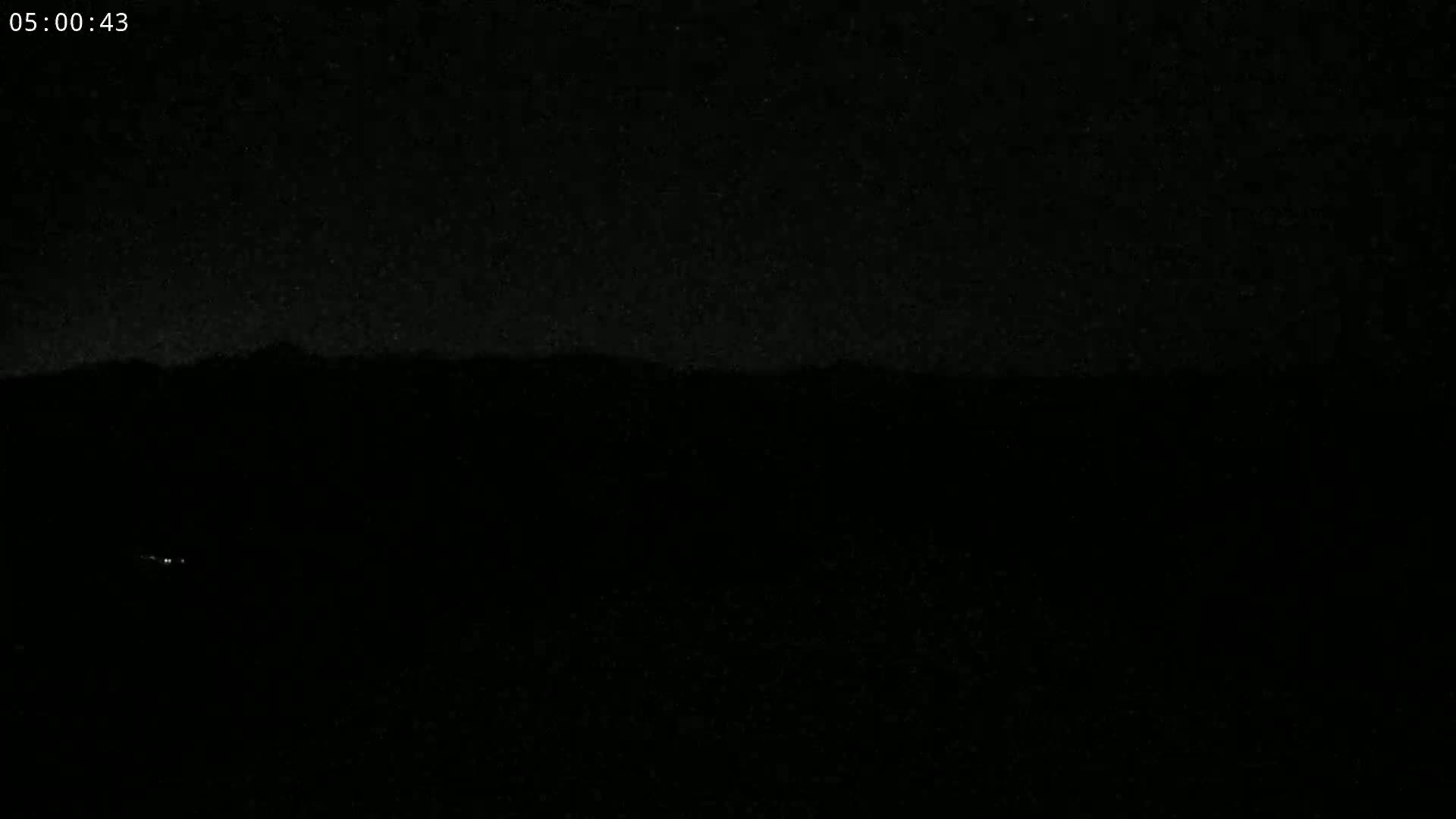 A dark, nighttime scene shows a distant, silhouetted mountain range under a star-filled sky.