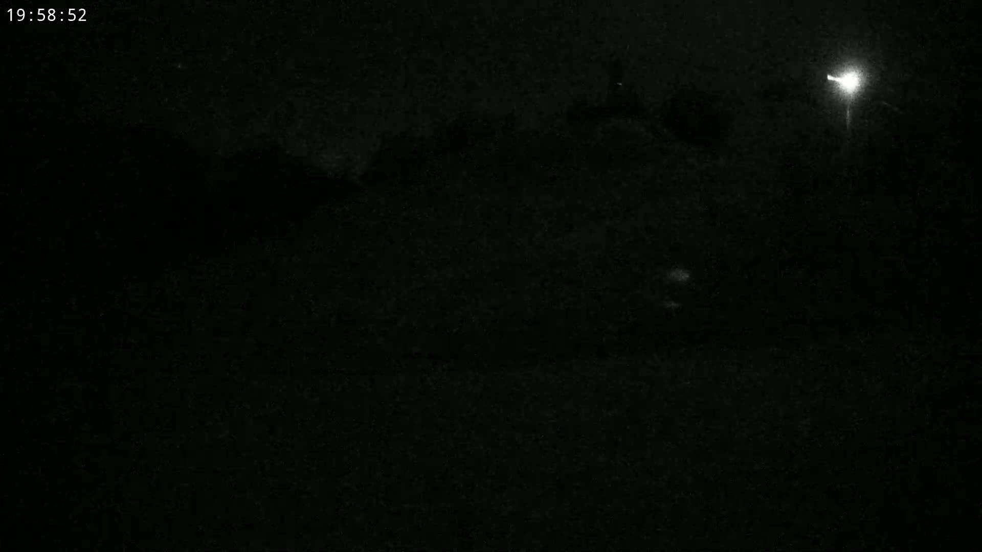 A nighttime outdoor scene shows a dimly lit area with a bright light source in the upper right corner.