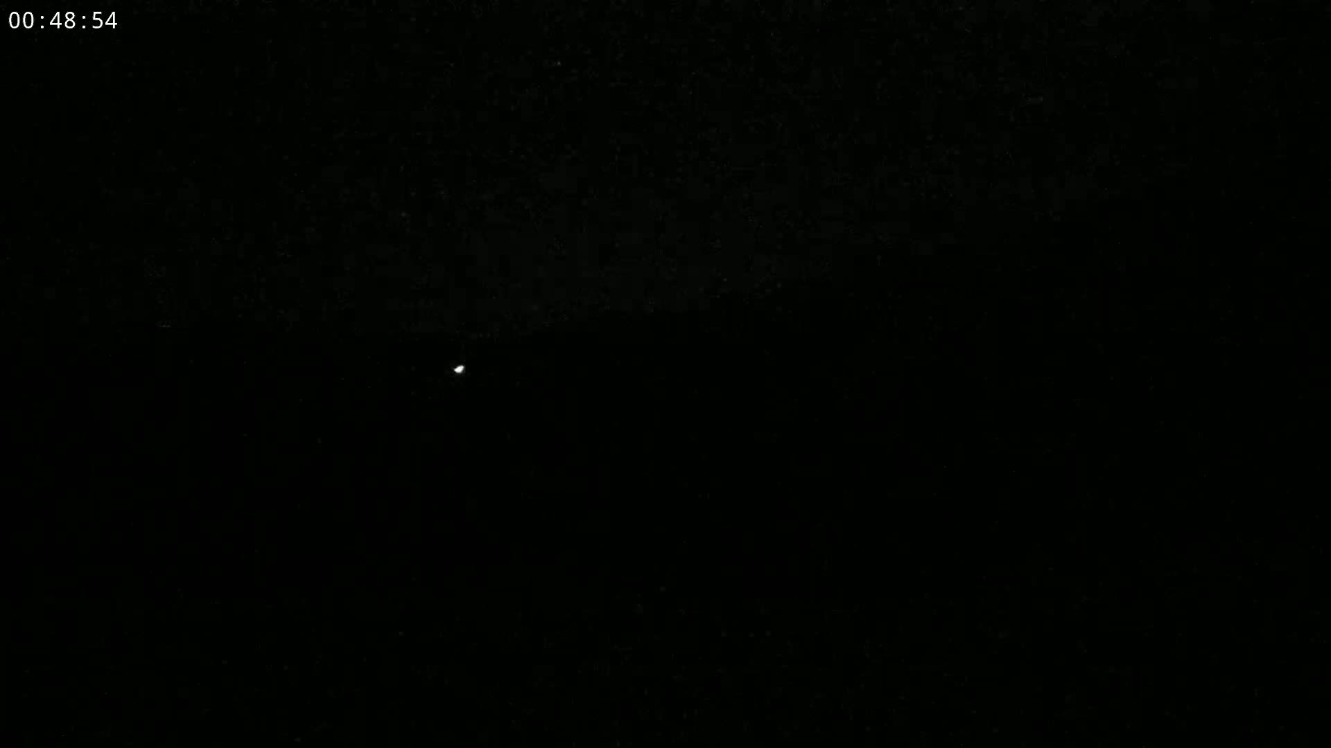 A small, bright light is visible in the center of a completely dark, nighttime scene.
