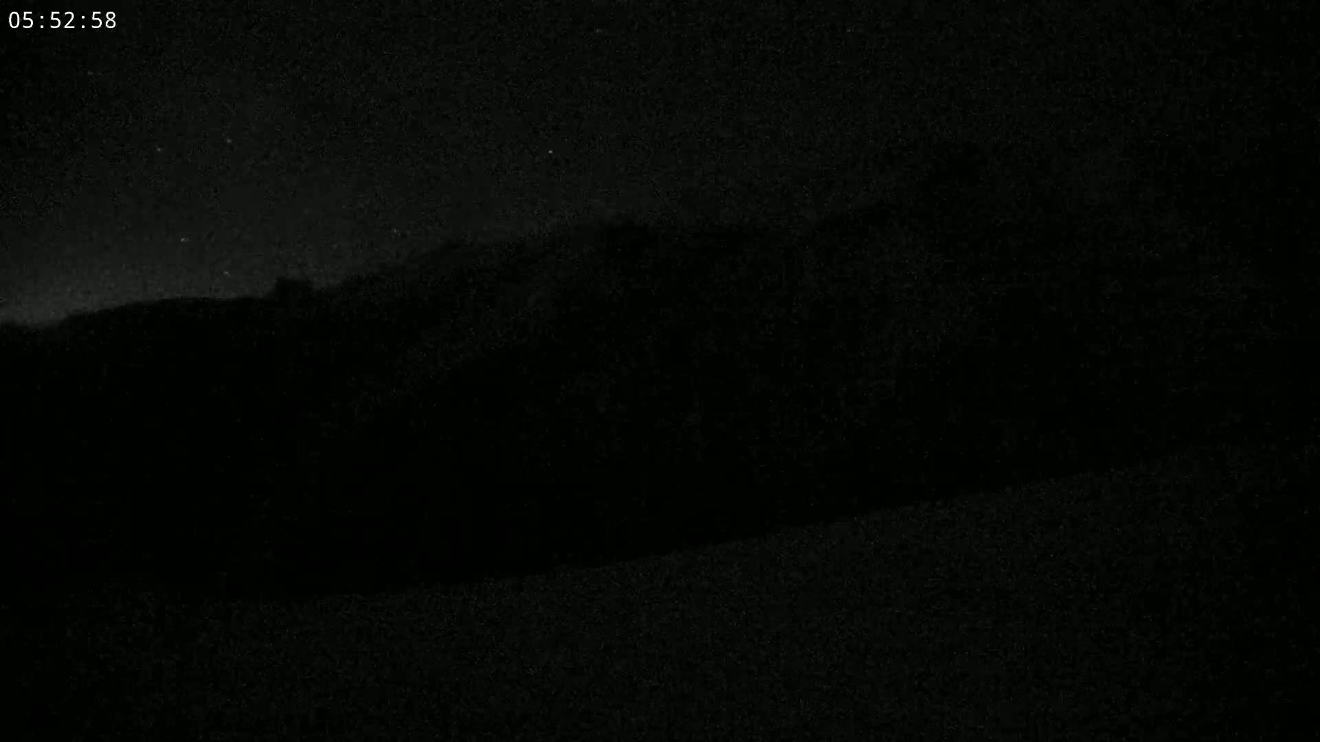 A dark, nighttime landscape shows a silhouetted hill or mountain range under a mostly clear sky.