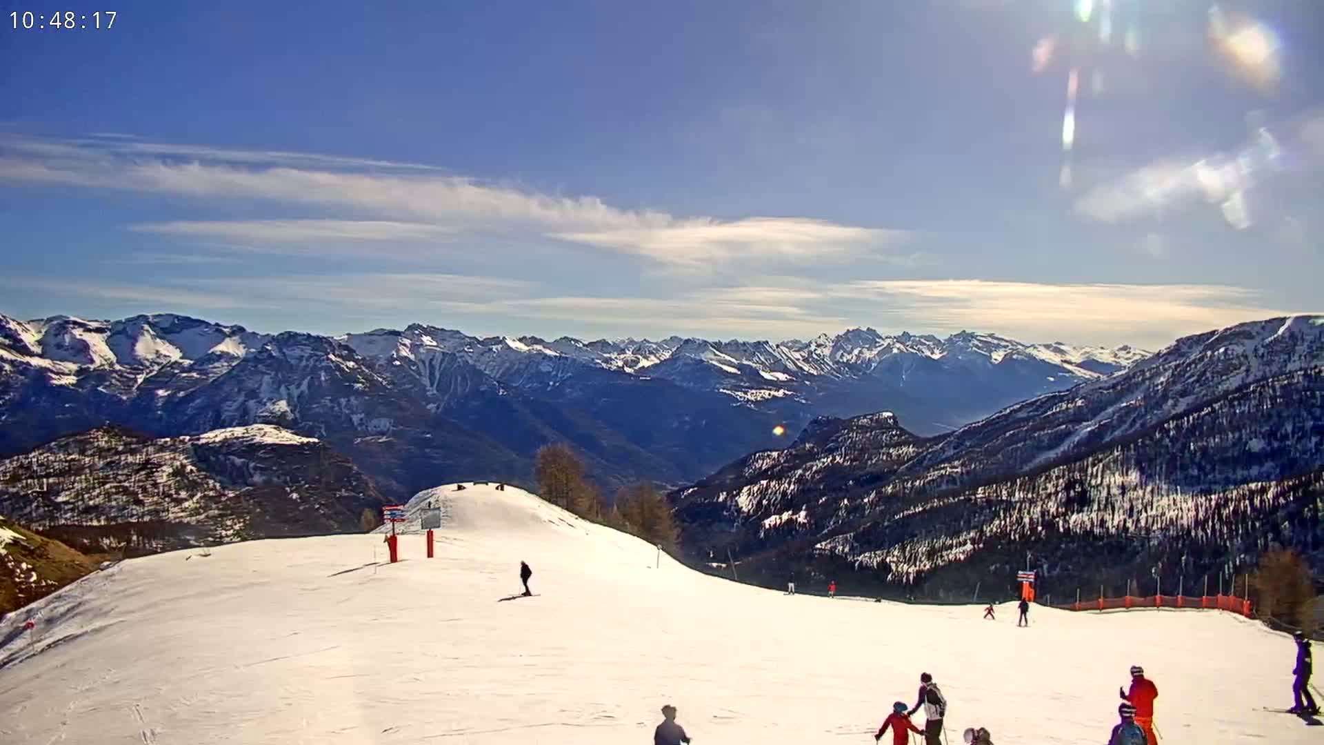 A sunny day on a snow-covered ski slope with a view of snow-capped mountains in the background.