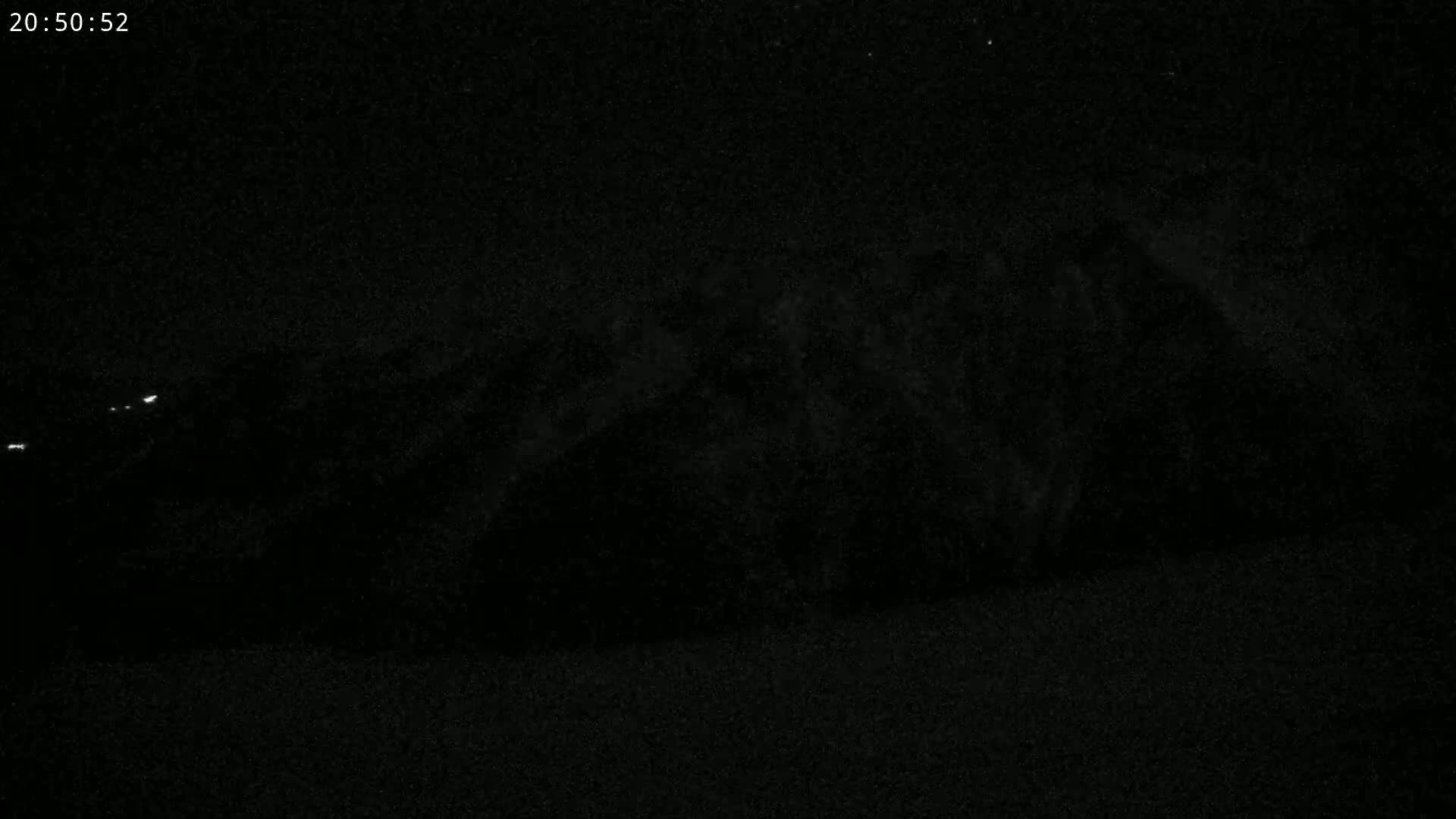 A dark, nighttime scene shows a blurry, indistinct landmass with a few faint lights in the distance.