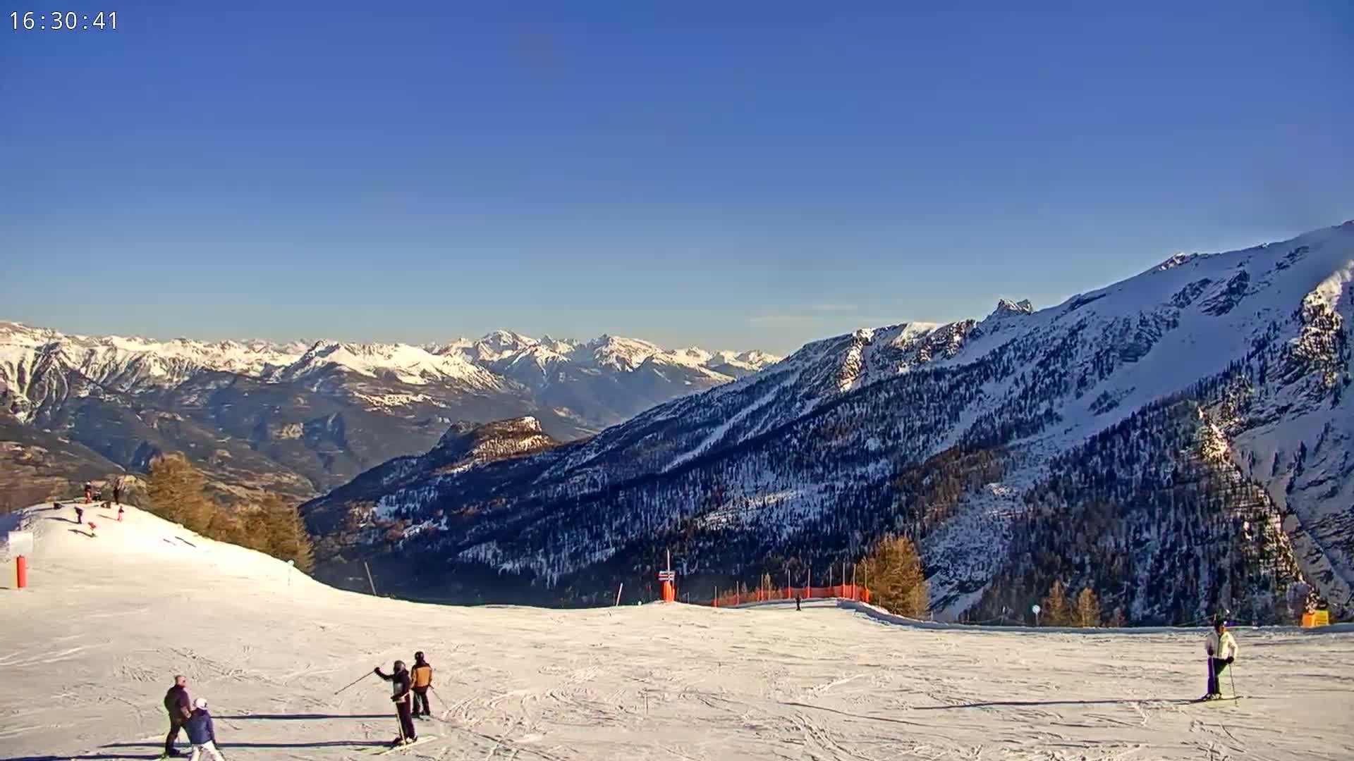 A sunny day on a snow-covered ski slope overlooking a vast range of snow-capped mountains.