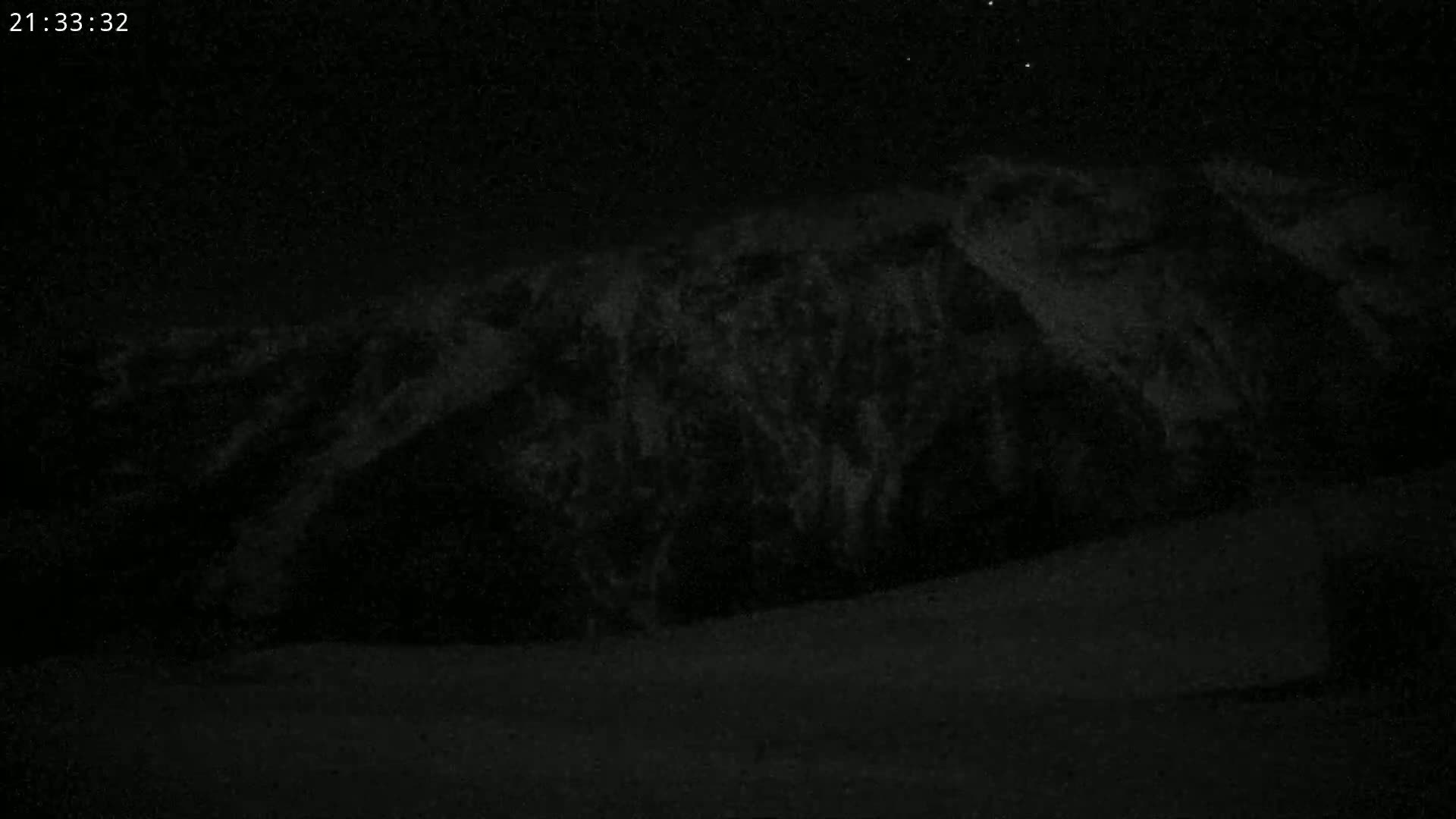 A dark, snow-covered mountain is visible under a clear night sky.