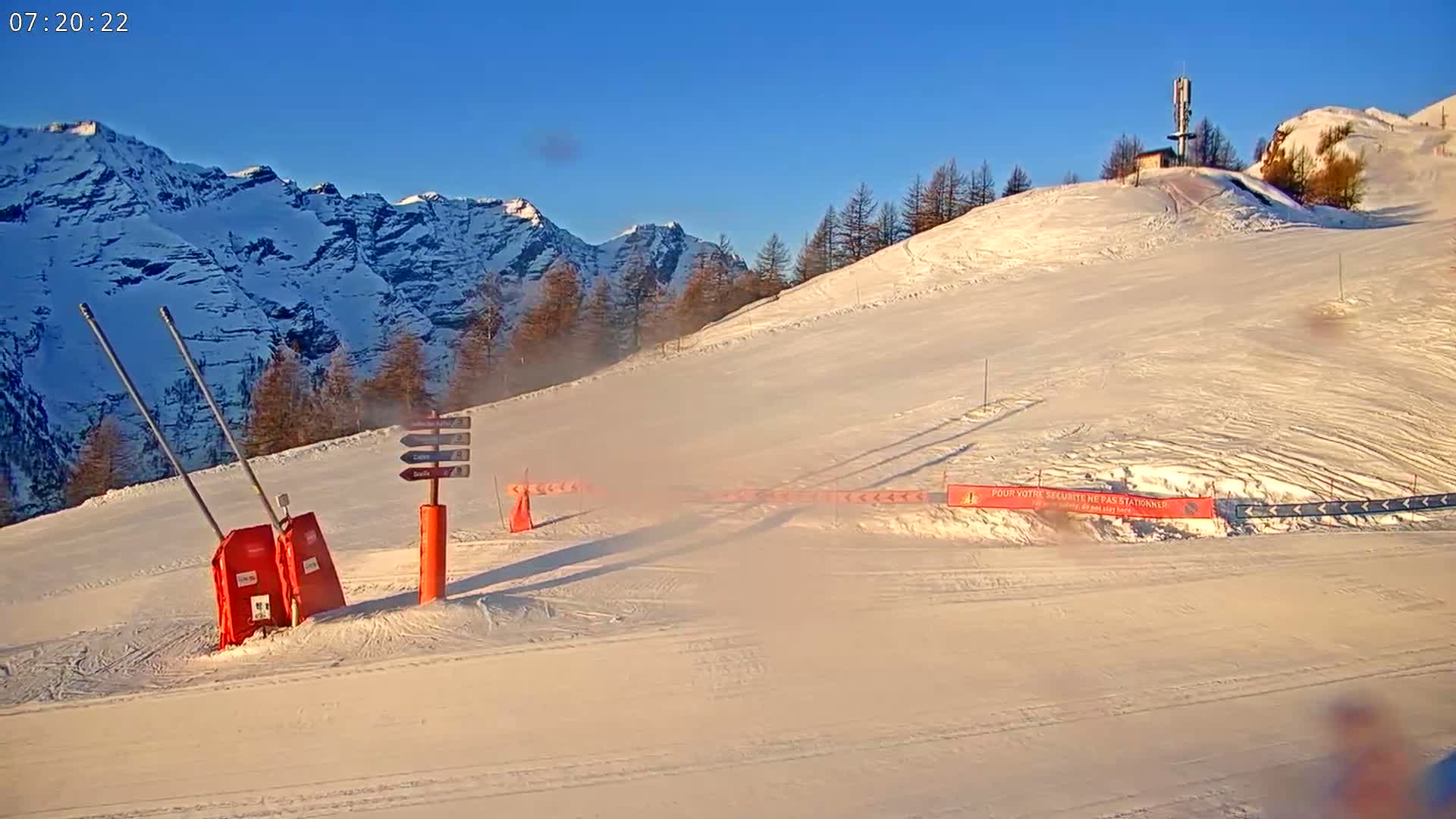 A snow-covered ski slope with a mountain backdrop under a clear, sunny sky.