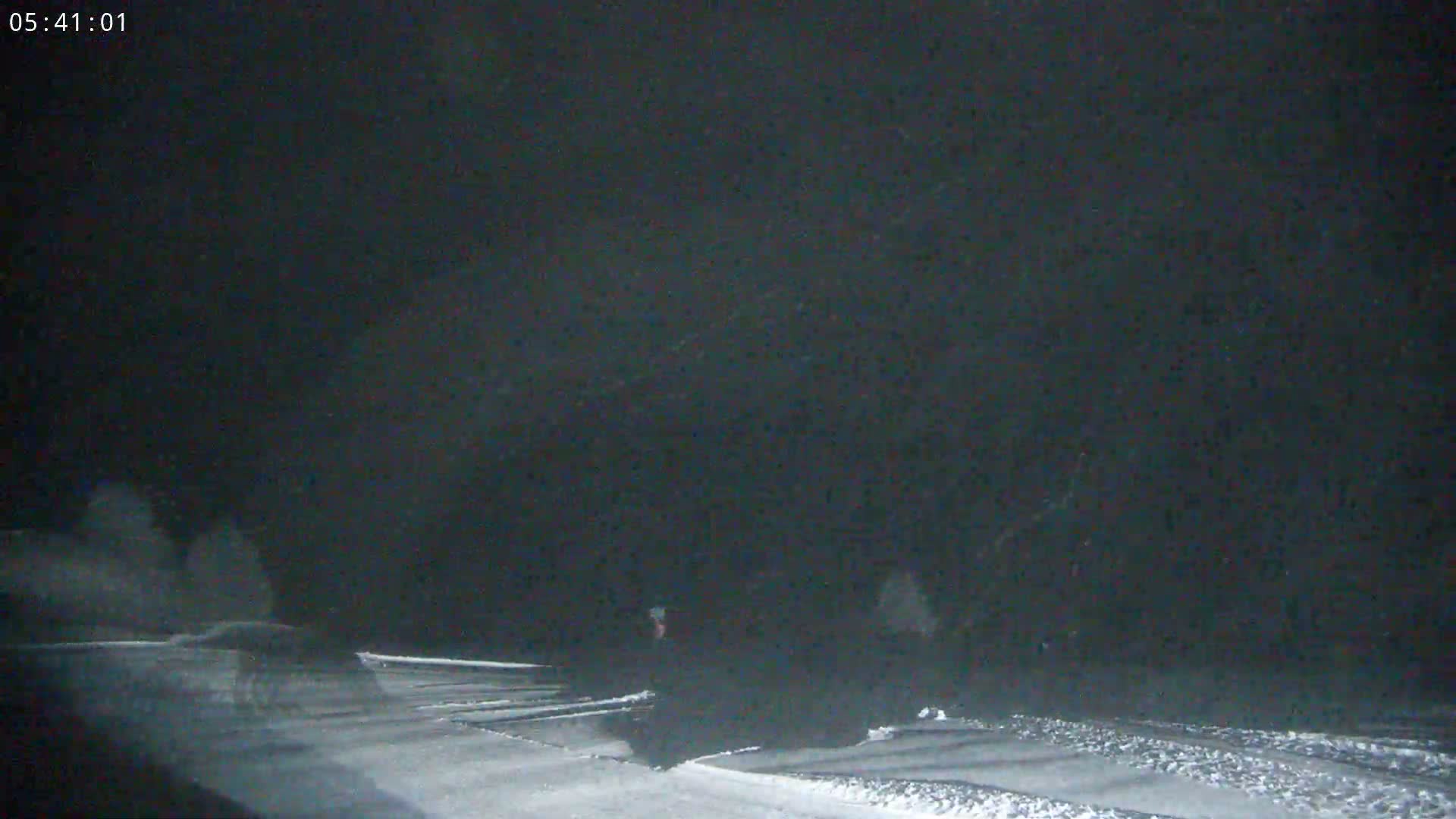 A dark, snowy scene at night shows indistinct figures moving across a snow-covered ground under falling snow.