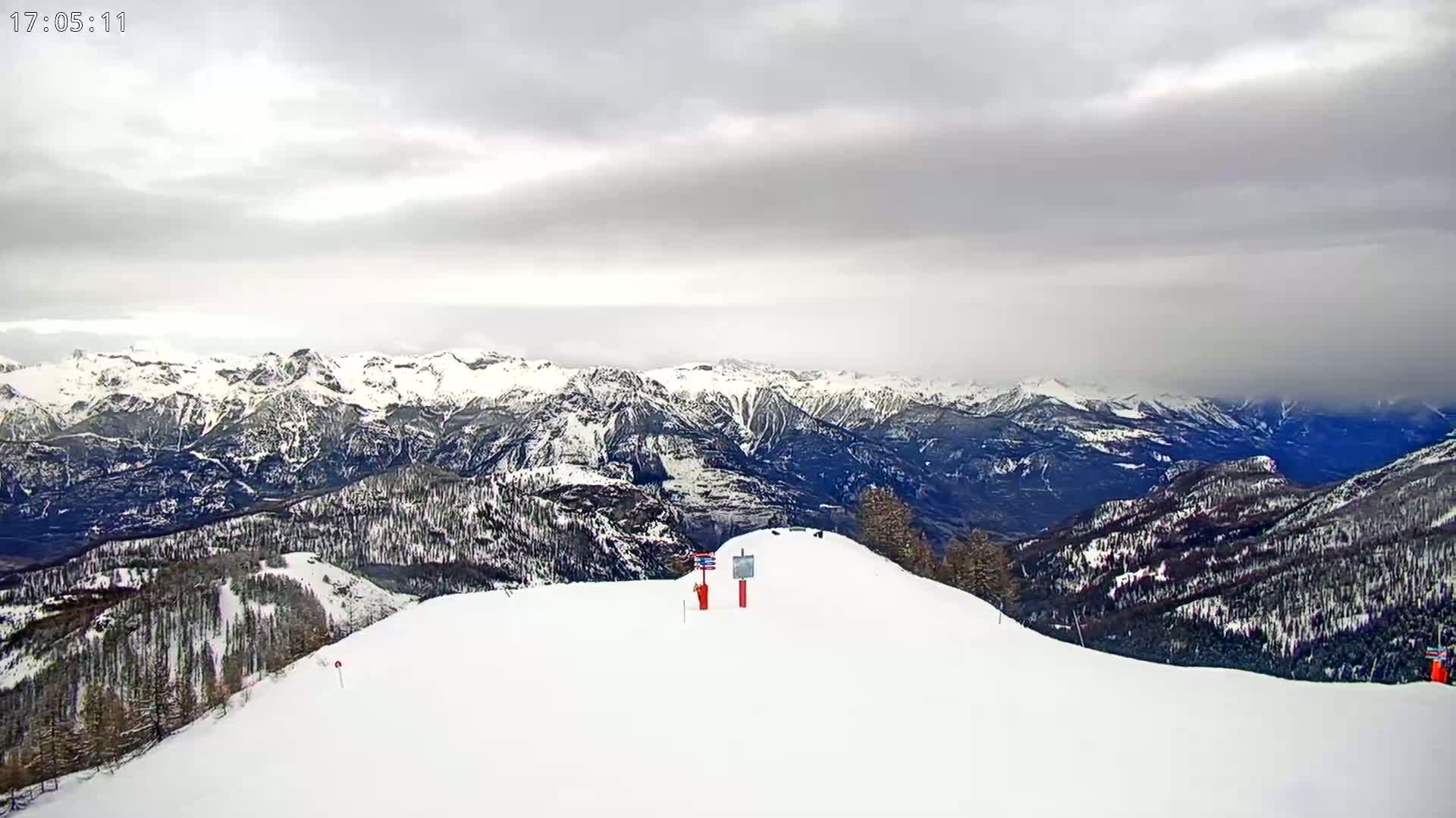 A snow-covered mountaintop overlooks a vast range of snow-capped mountains under an overcast sky.
