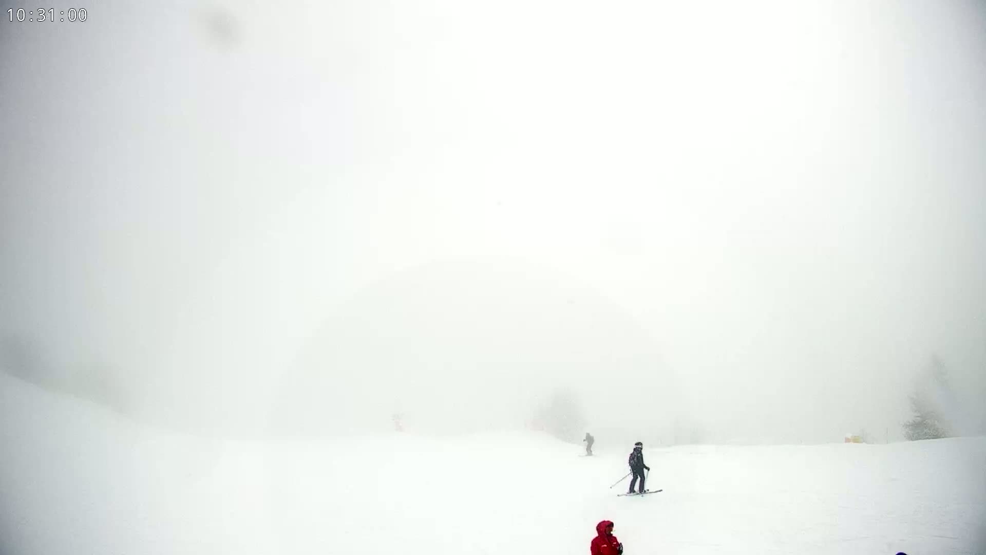A snowy, foggy ski slope with several skiers visible in the distance.