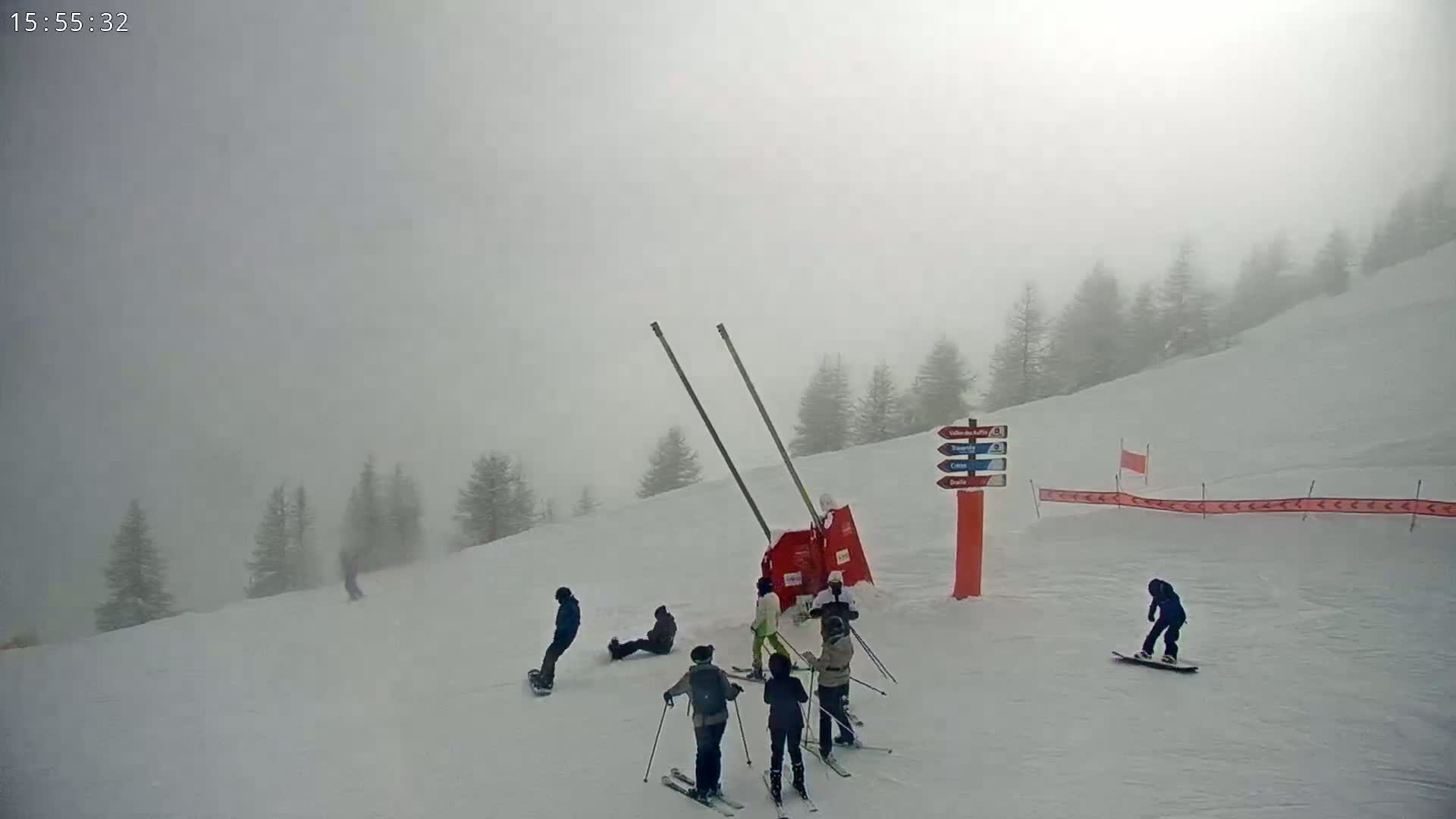 A snowy ski slope shrouded in fog, with several skiers and snowboarders present near a ski lift.