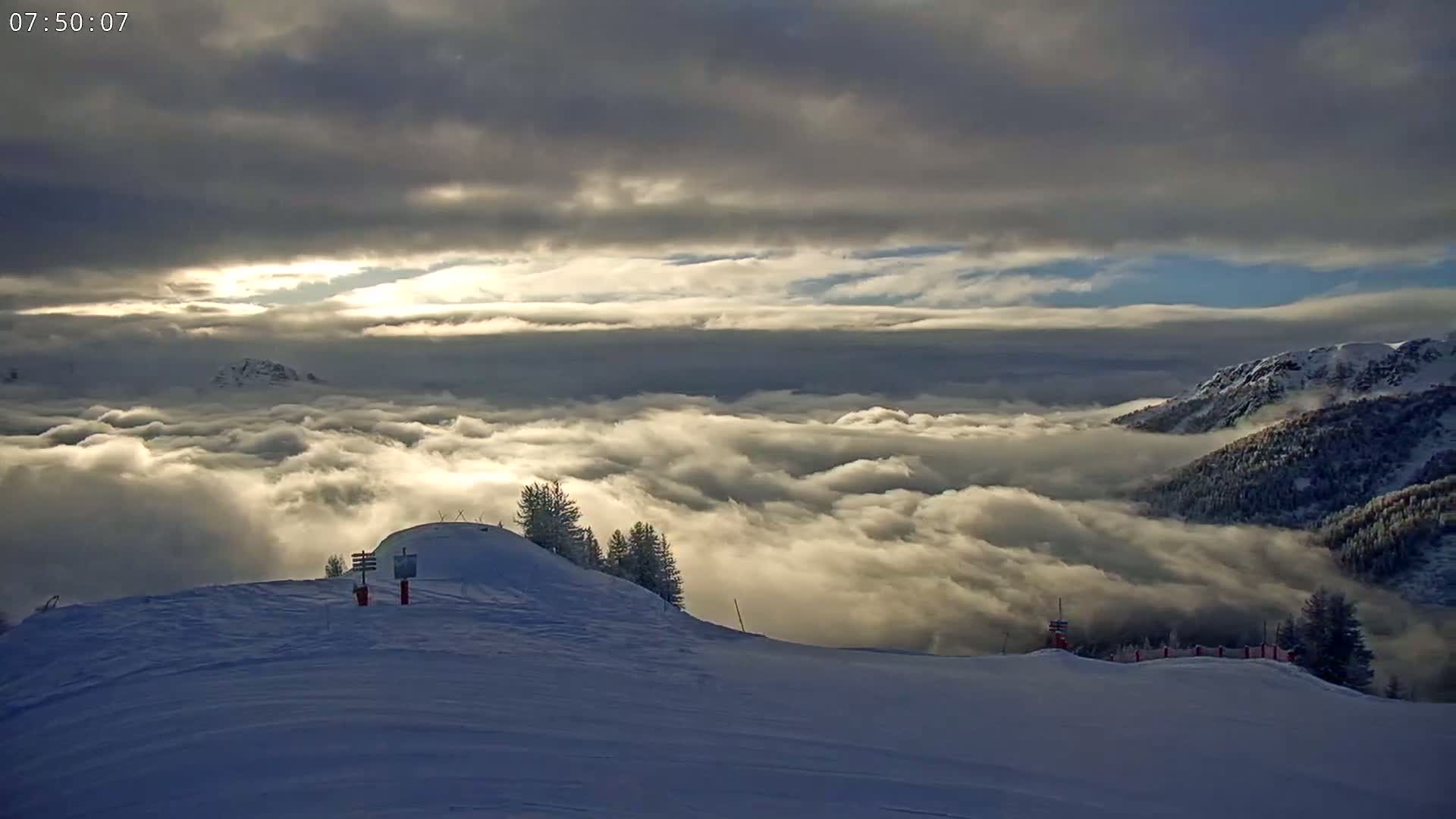 A snowy mountaintop overlooks a vast expanse of clouds illuminated by the rising sun, with dark clouds above.