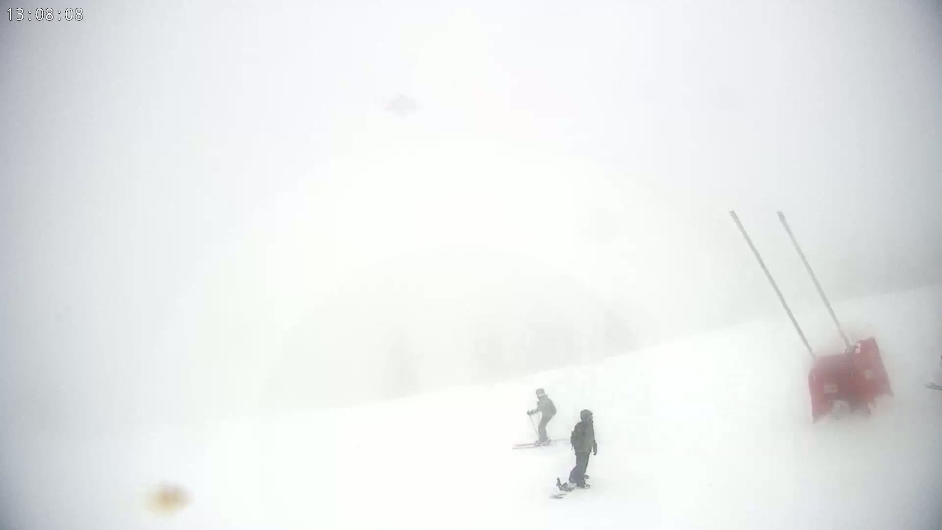 Two skiers are visible on a snowy slope in heavy fog.