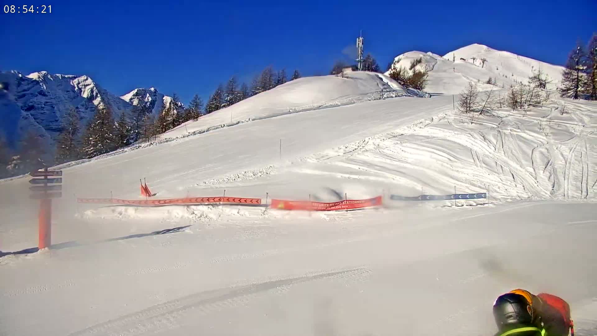 A snowy ski slope with a mountain in the background under a clear blue sky.