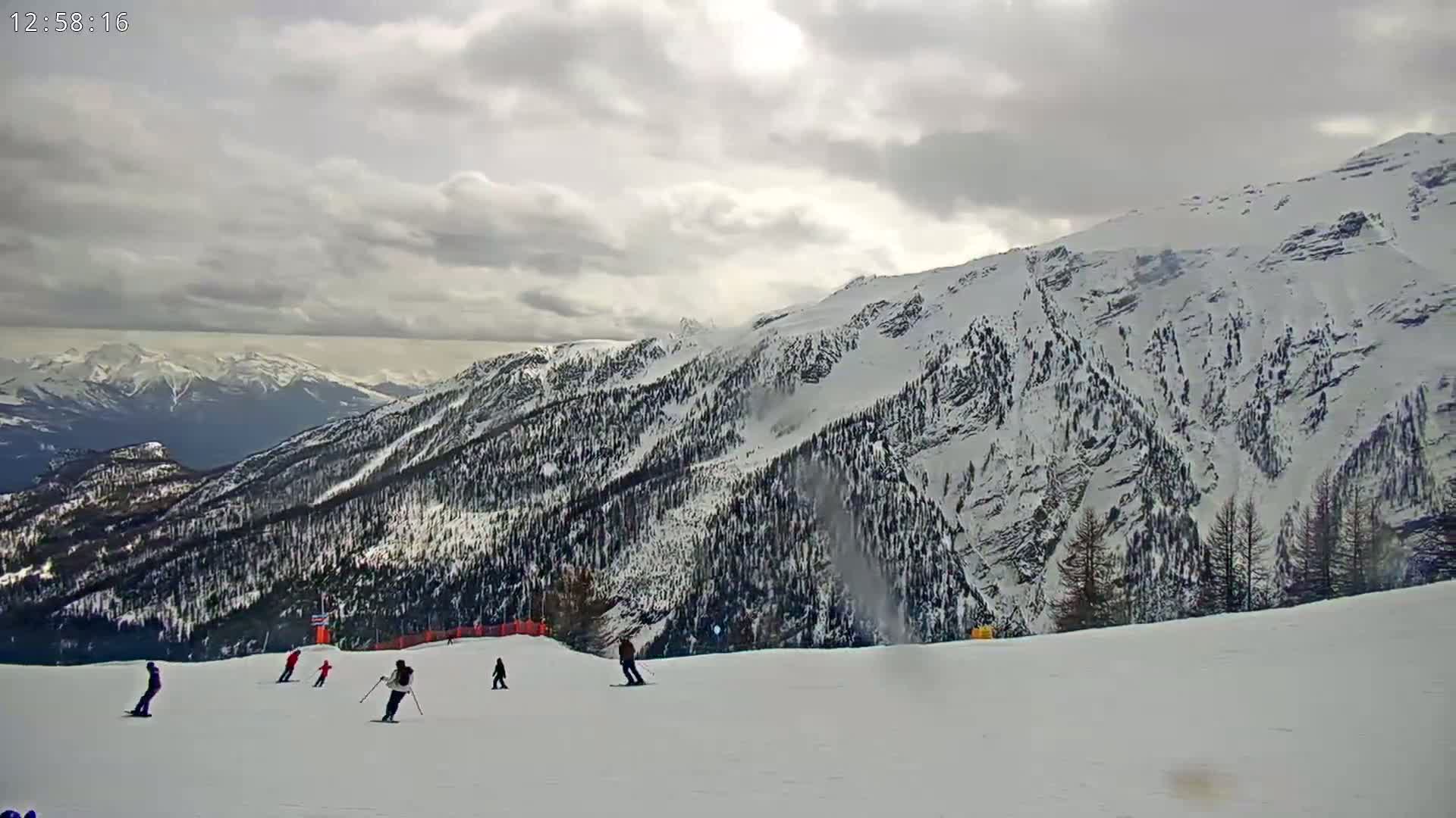 A snowy mountain slope with several skiers on a mostly clear, overcast day.