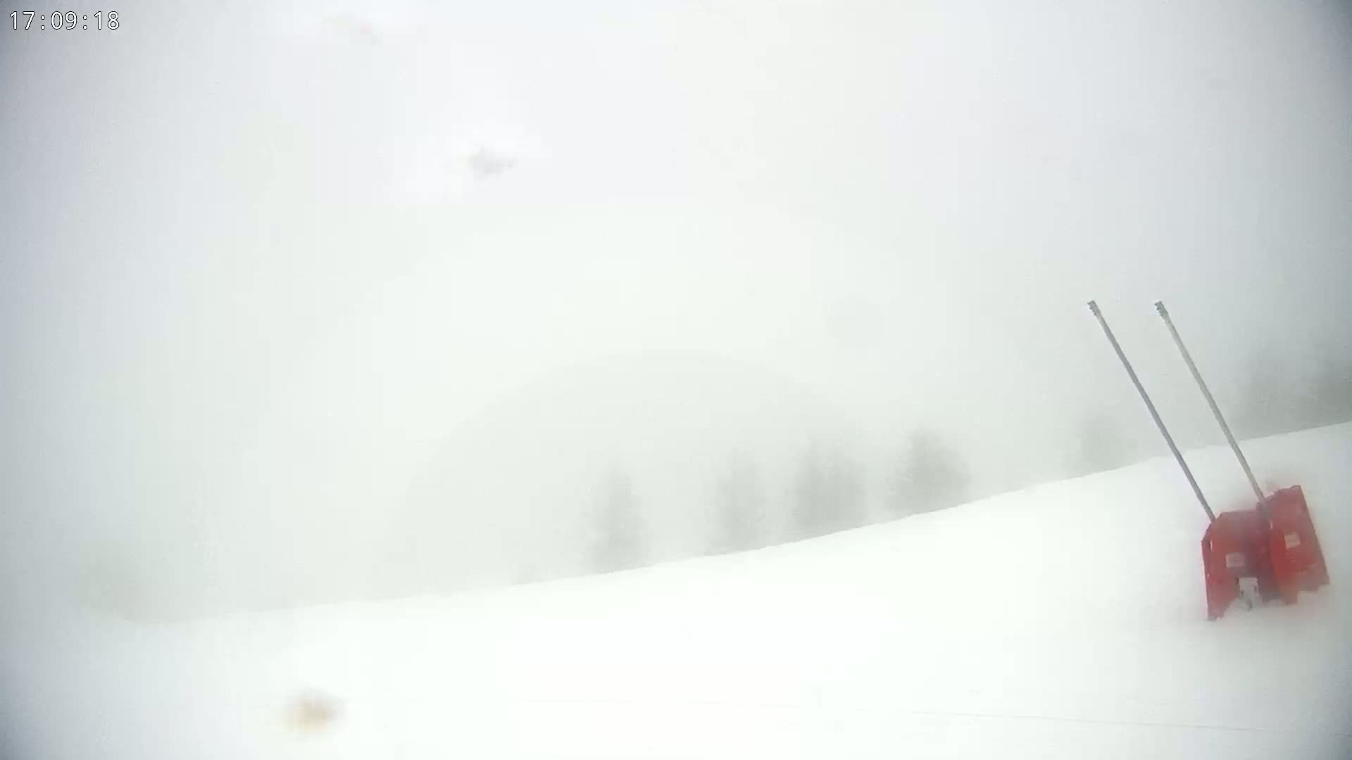 A snowblower sits on a snow-covered slope in heavy fog.