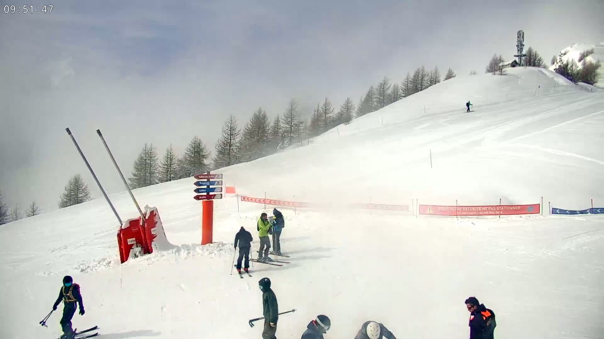 A snowy ski slope with several skiers and snowboarders, under a hazy, overcast sky.