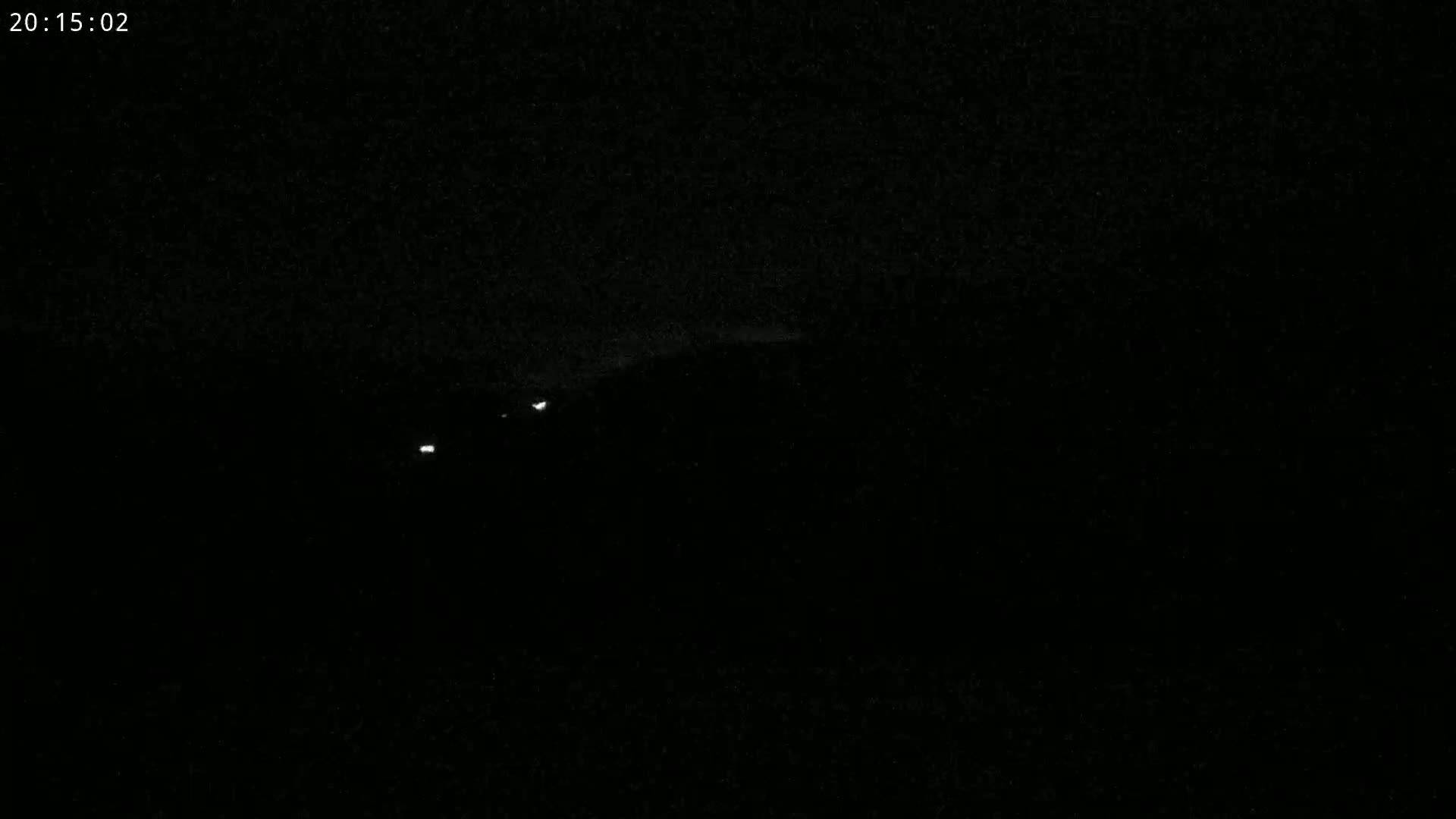 A nighttime, dark image shows a few faint lights in the distance.